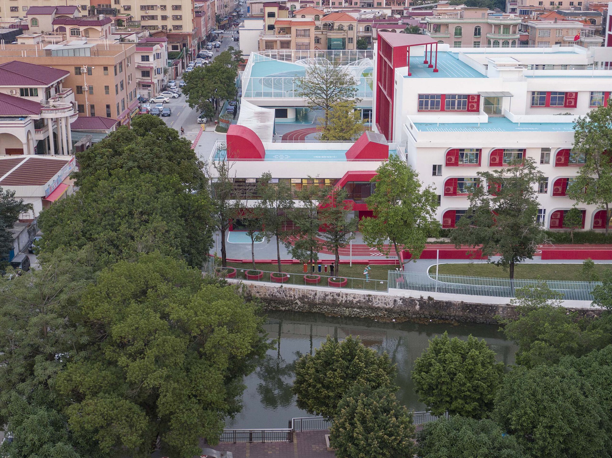 Campus buildings with red accents and white volumes set along a tree-lined canal at twilight
