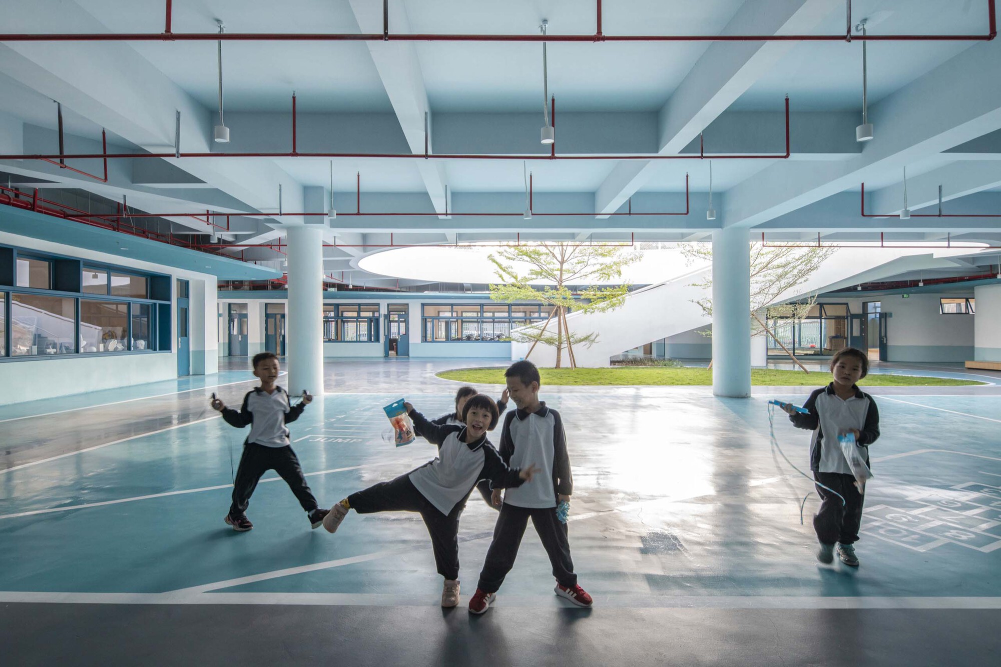 Covered courtyard with exposed blue-painted beams and columns where children play near a central tree