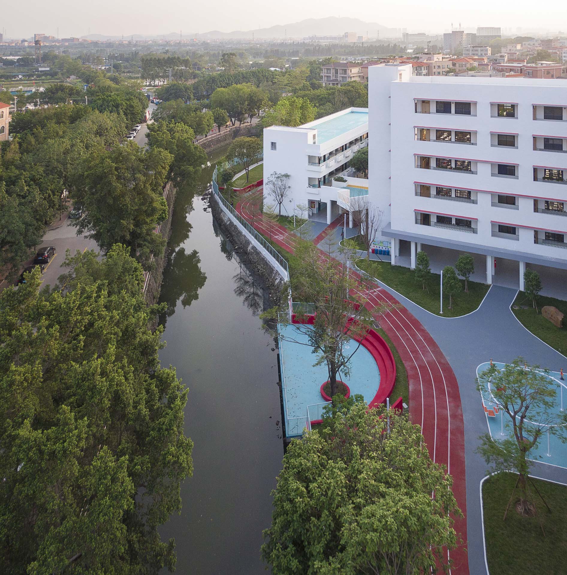 Aerial view of the red running track curving along the canal with white classroom block at dusk