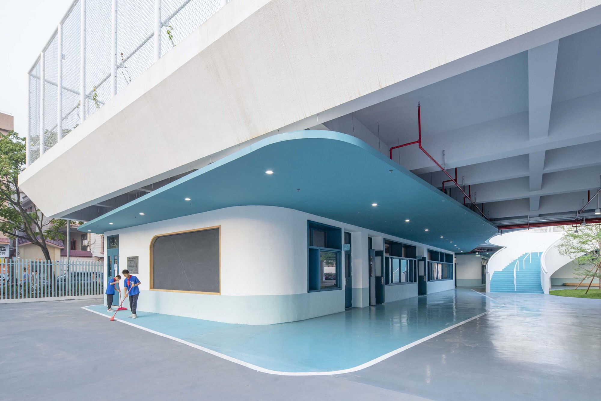 Covered ground floor corridor with curved turquoise soffit and two children walking near the entrance
