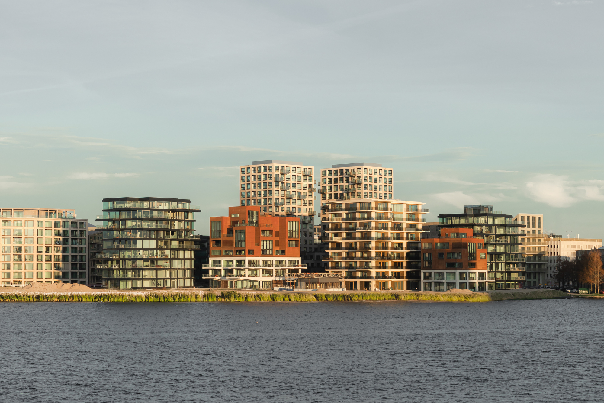 Waterfront view of mixed-height residential blocks with brick and metal cladding at sunset