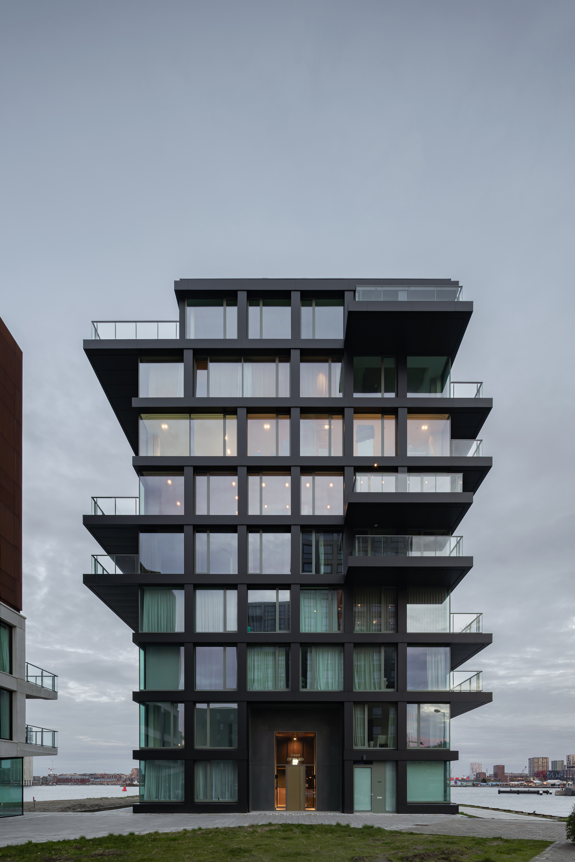 Glass tower with deep black balconies and illuminated interiors at dusk