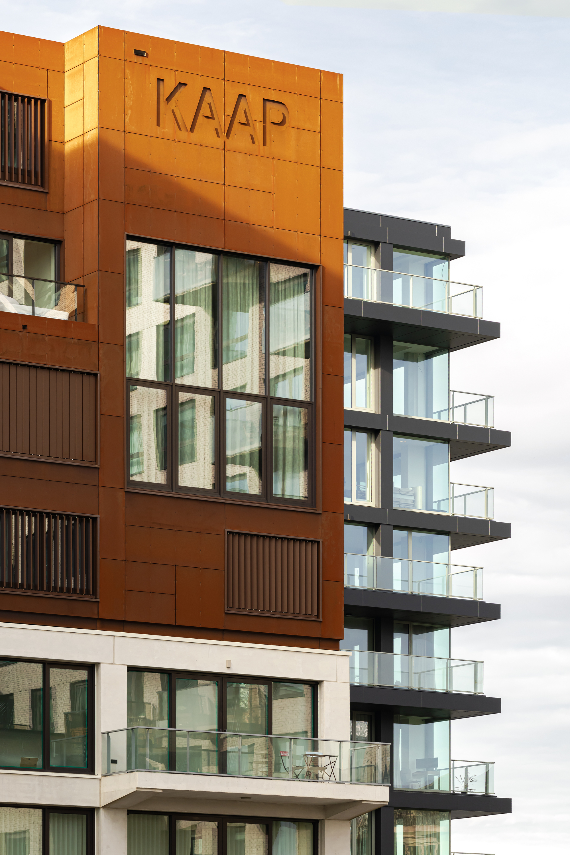 Weathered steel facade panel with incised lettering and vertical louvres beside glass tower