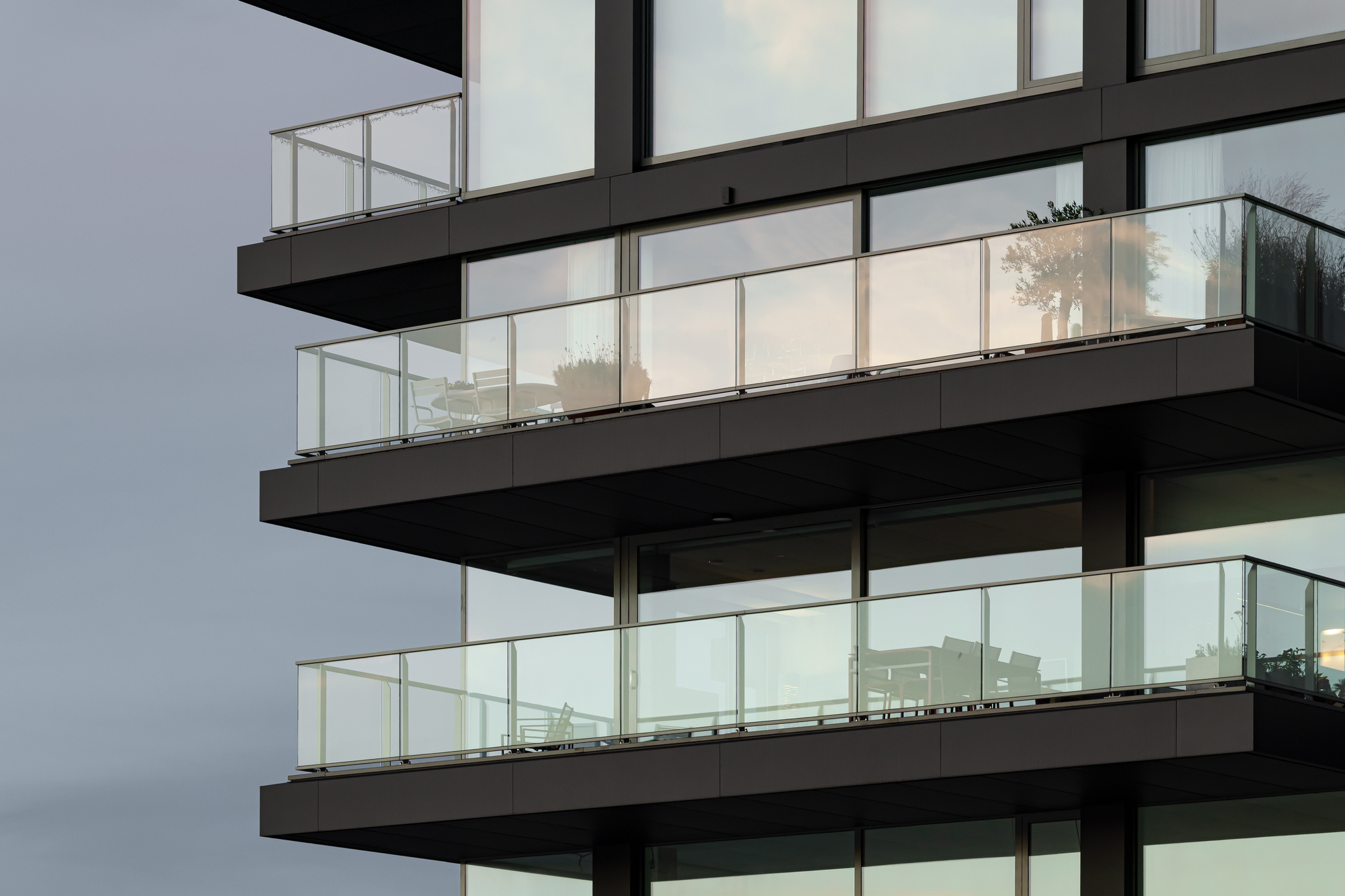 Stacked balconies with black metal parapets and glass railings at twilight