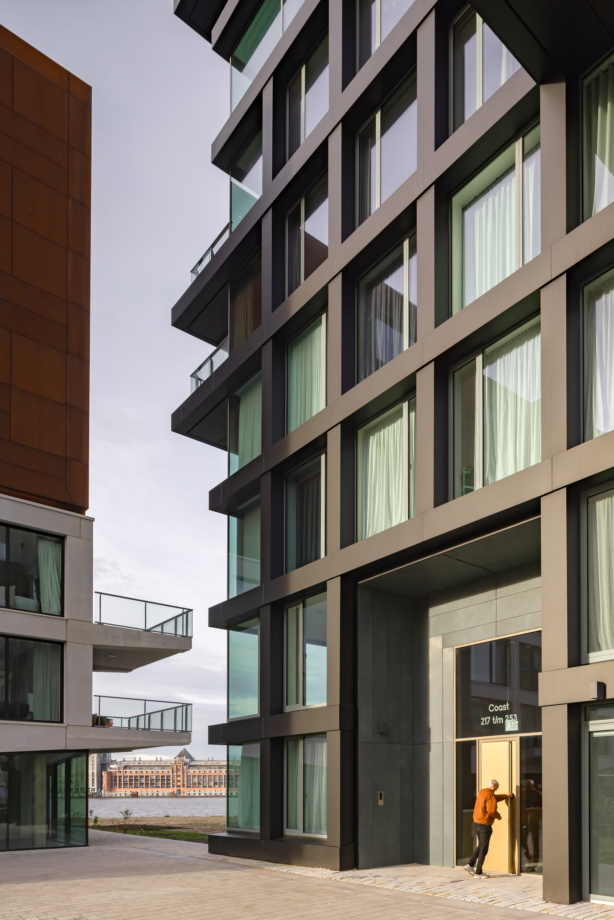 Street-level entrance between residential blocks with a person in orange jacket approaching under overcast sky