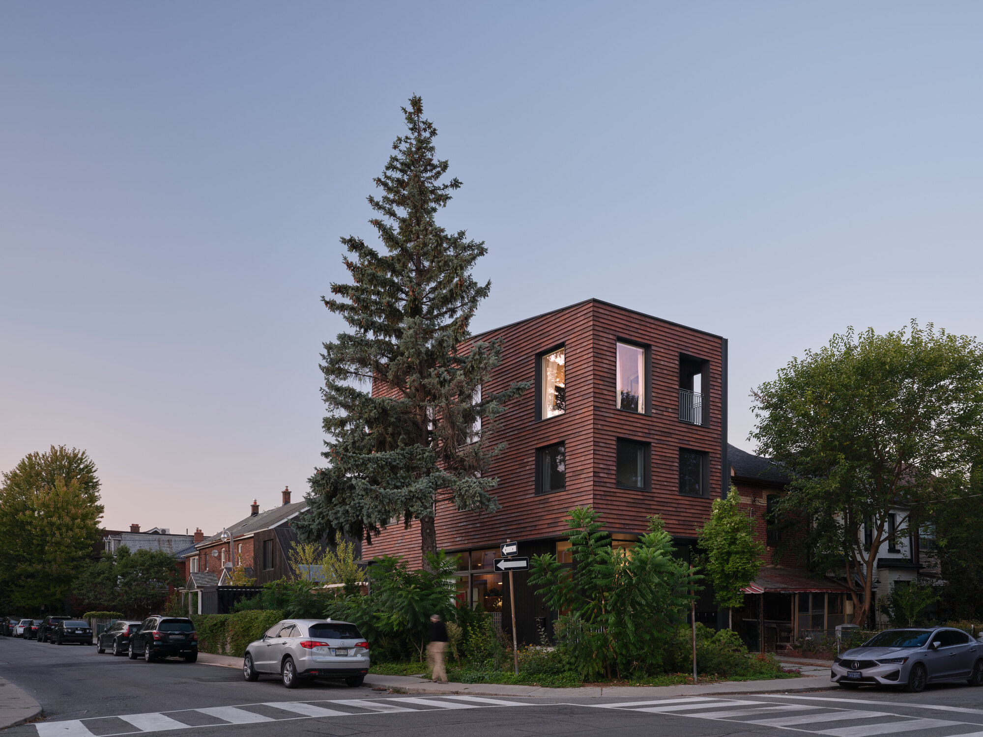 Corner view of the horizontal ribbed copper facade with a tall evergreen tree at dusk