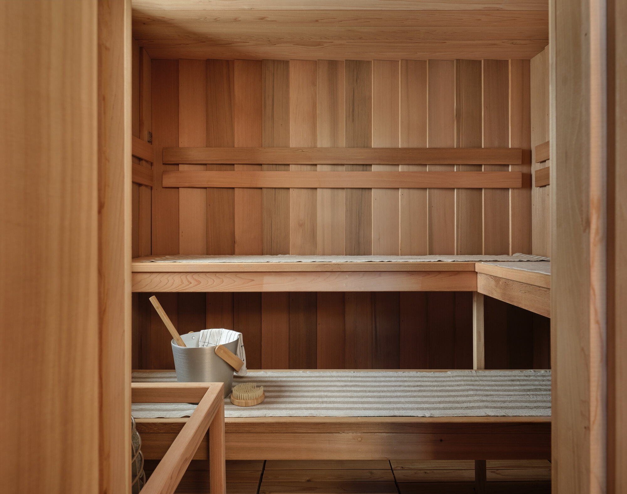 Cedar sauna interior with tiered benches, vertical paneling, and traditional bucket and ladle