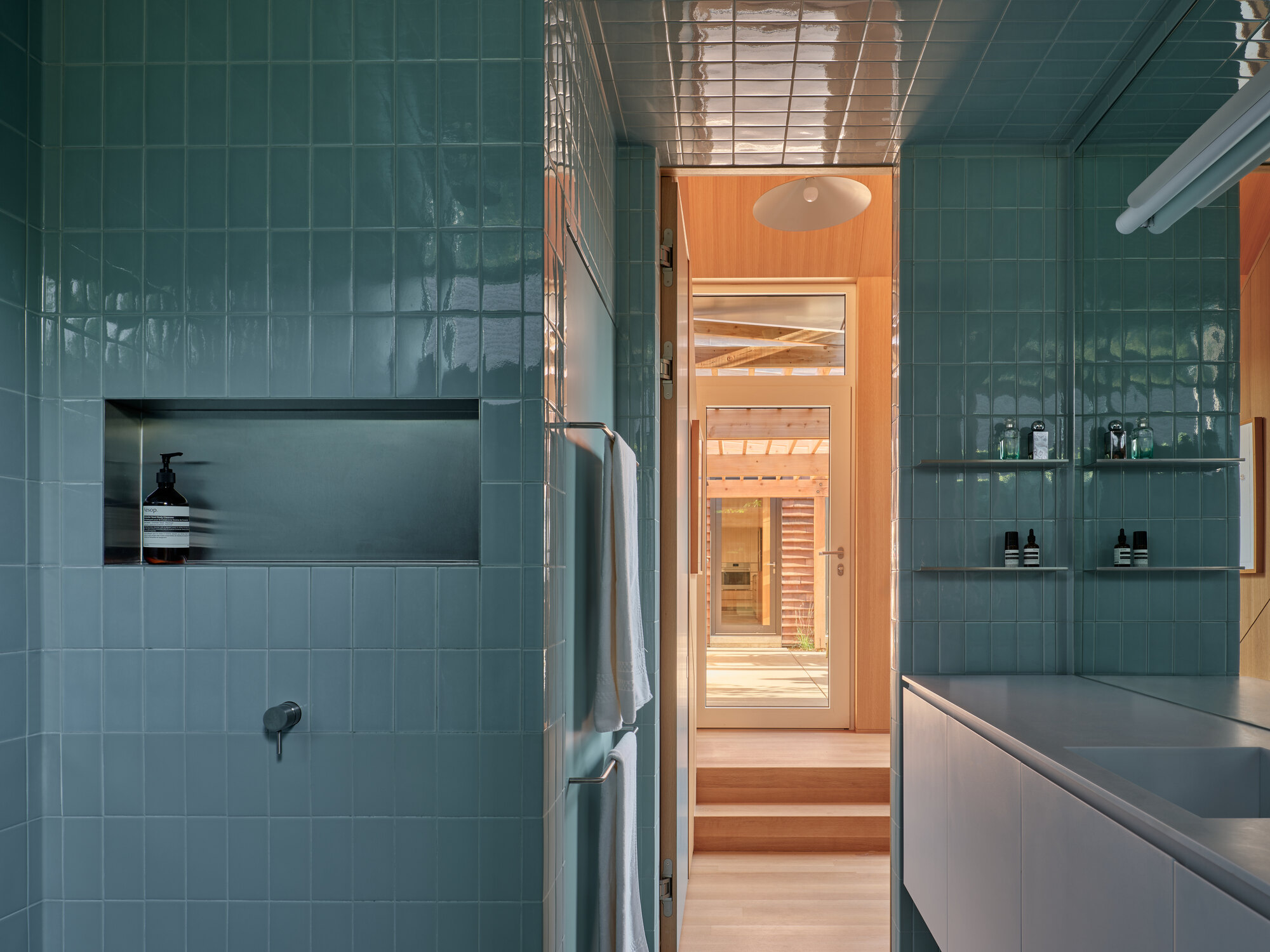 Green tile bathroom with recessed niche, glass shelving, and view through to the sauna beyond