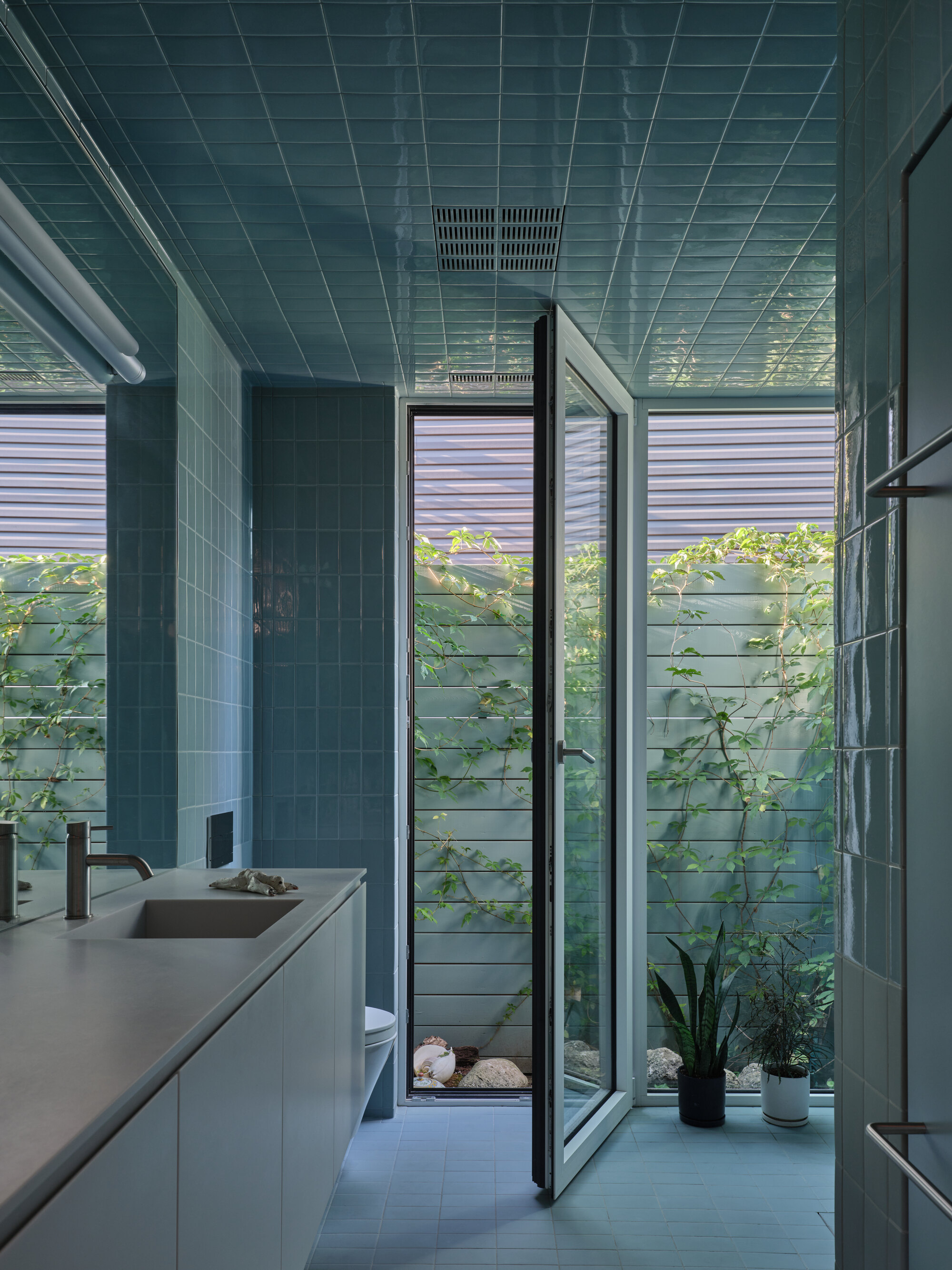 Tiled bathroom opening to a courtyard with climbing vines and horizontal timber fencing