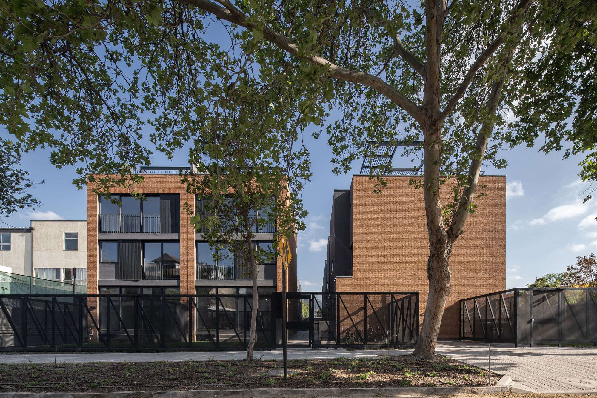 Street view of the brick facade with raised steel-braced ground floor beneath mature tree canopy