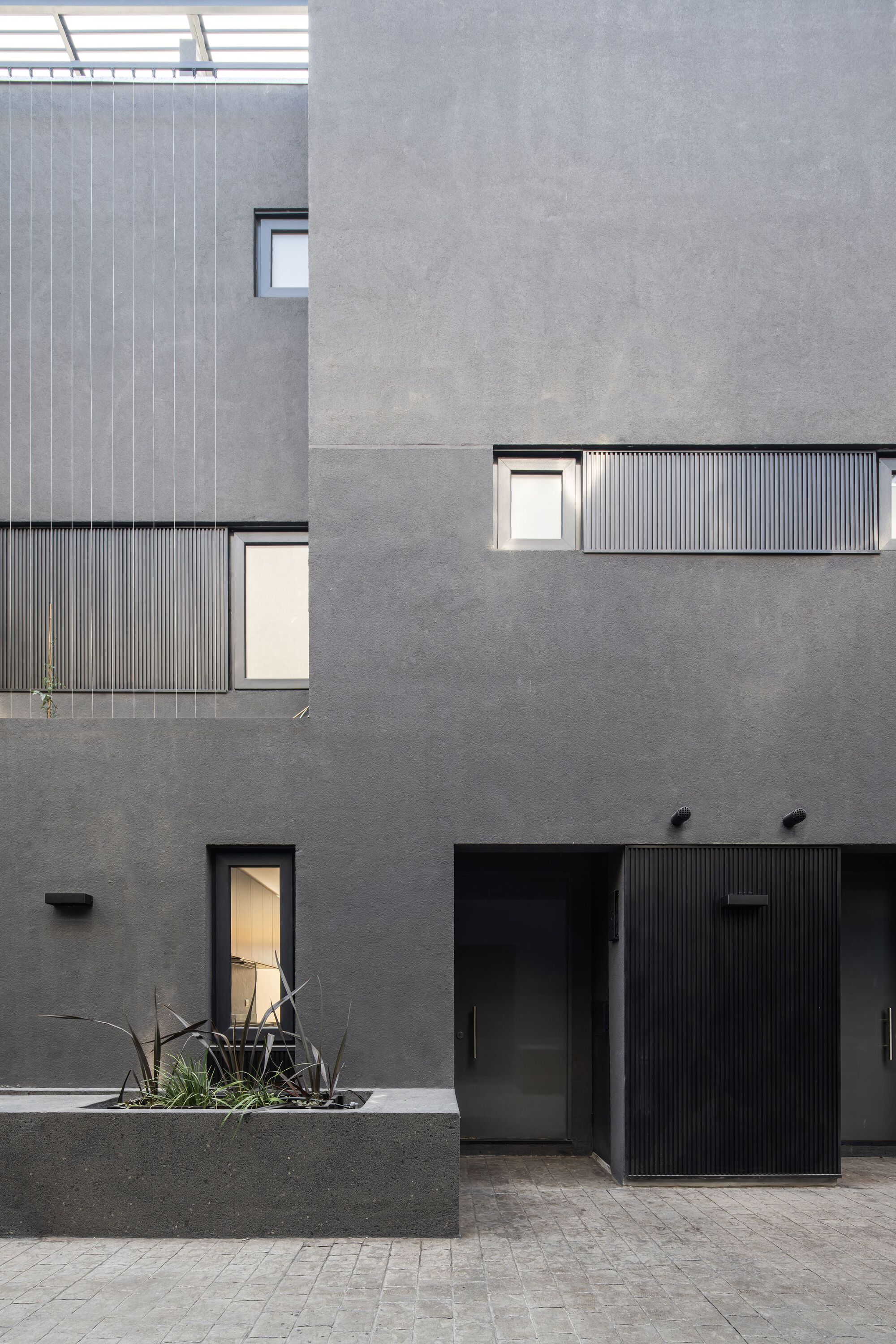 Courtyard facade composition with grey render, corrugated metal cladding panels and punched window openings