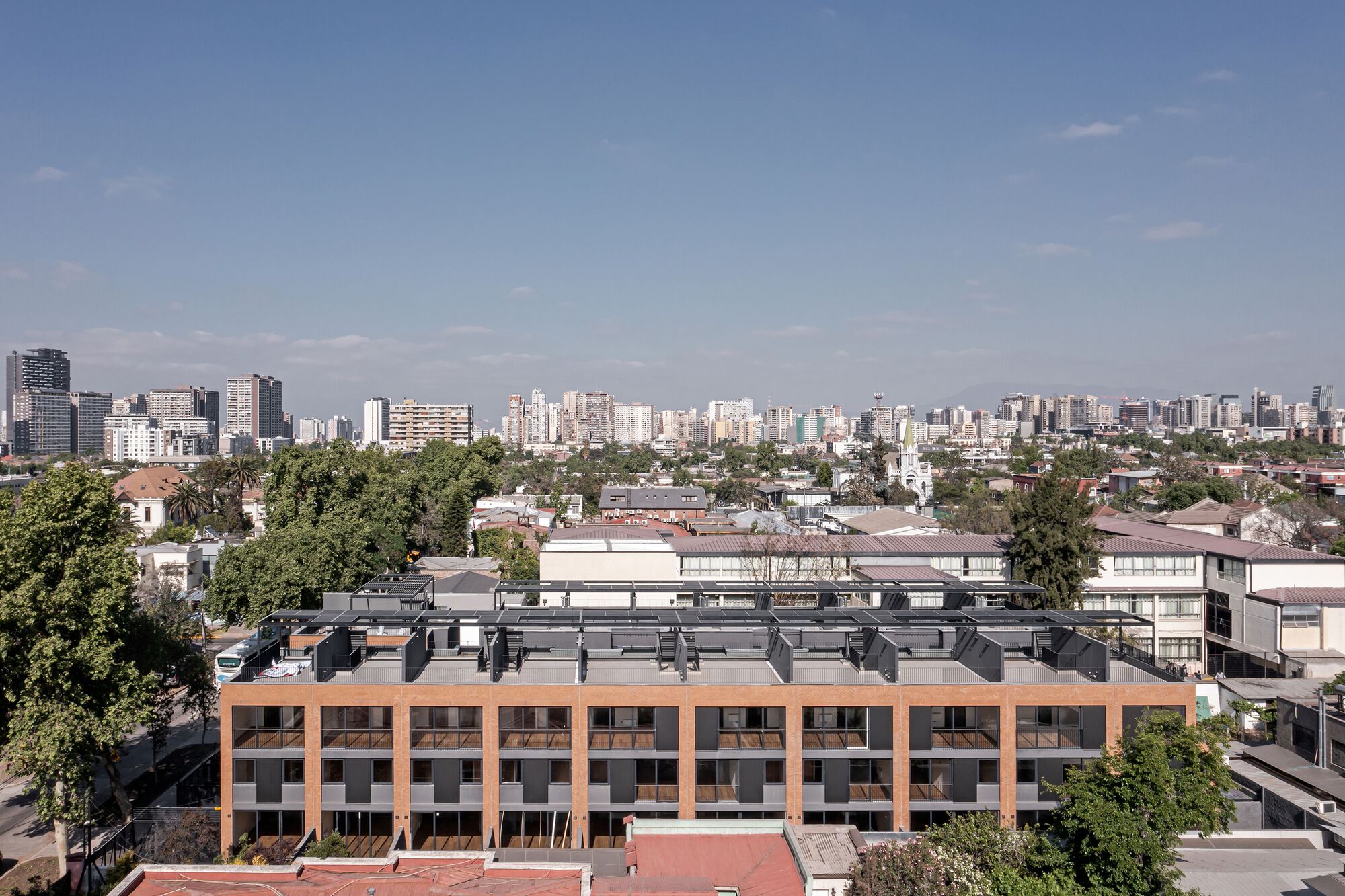 Elevated view of the brick and dark metal facade with rooftop solar panels against the distant skyline