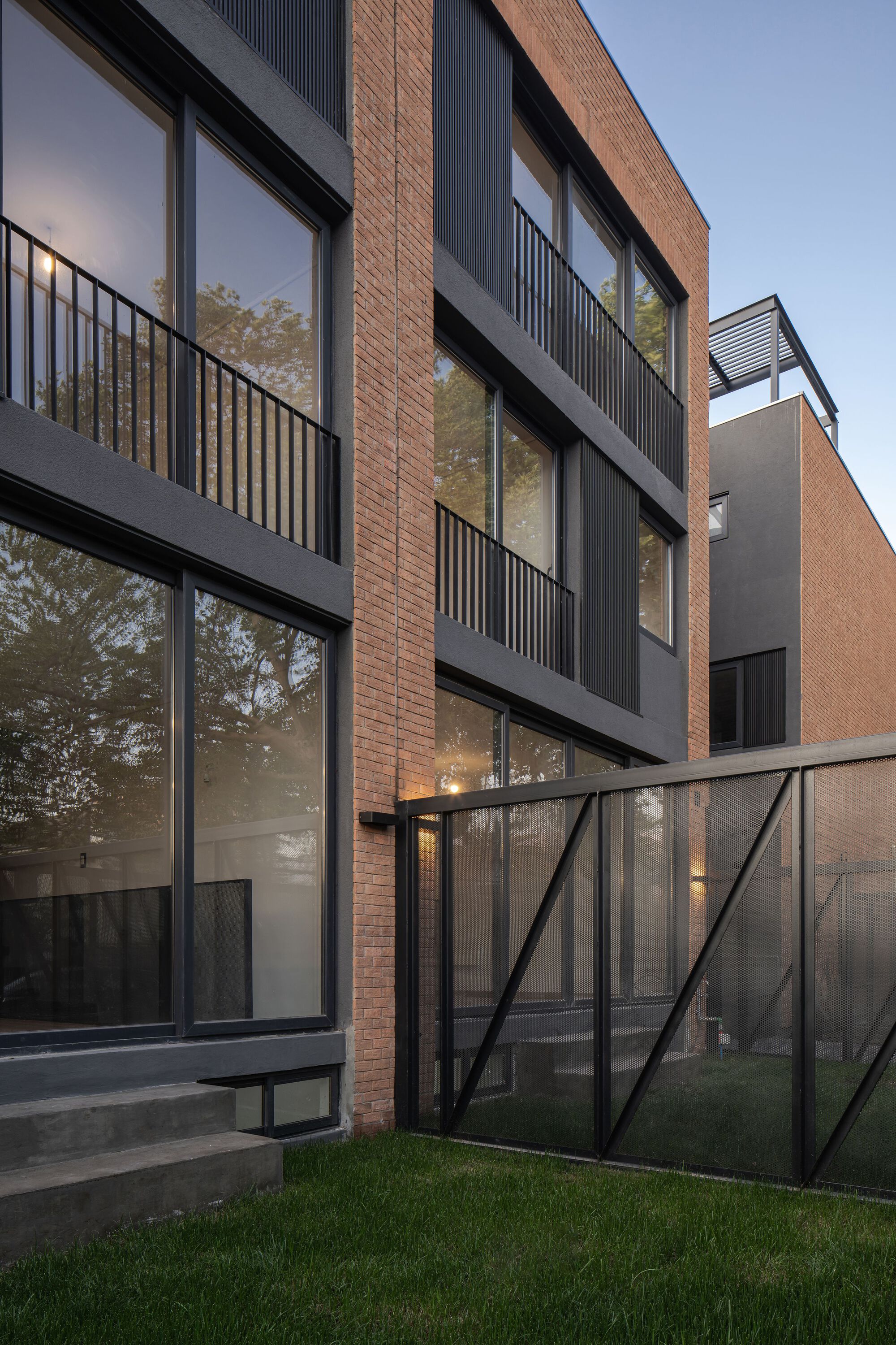 Facade detail with alternating brick and corrugated metal panels above a lawn and diagonal metal fence