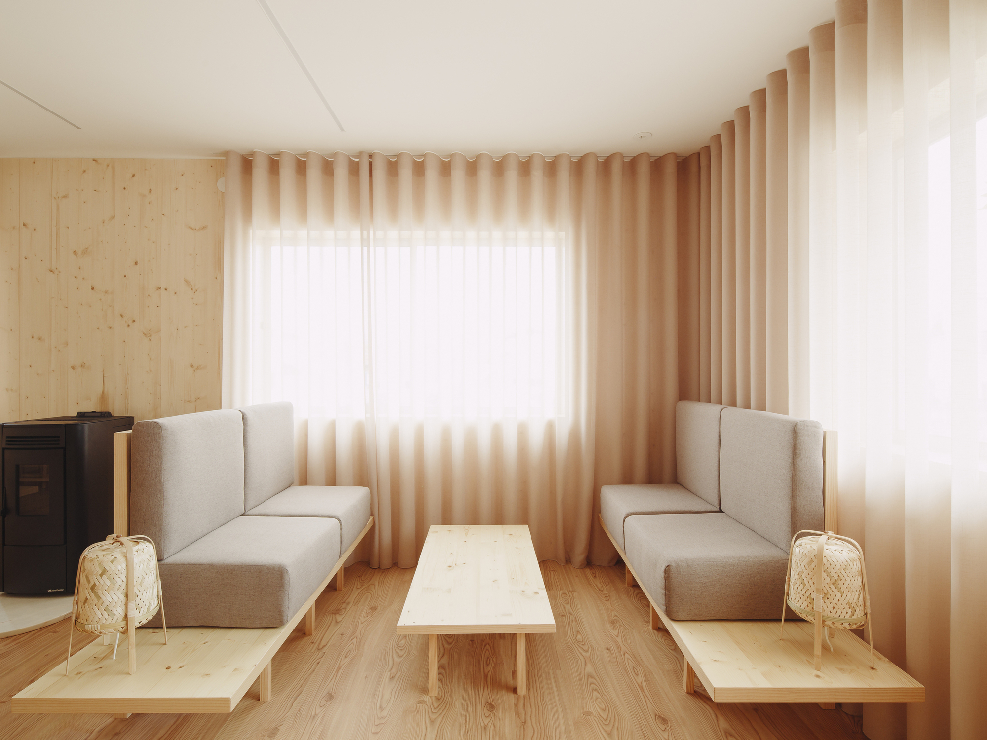 Corner seating area with upholstered benches and low table beneath pleated fabric curtains in warm light