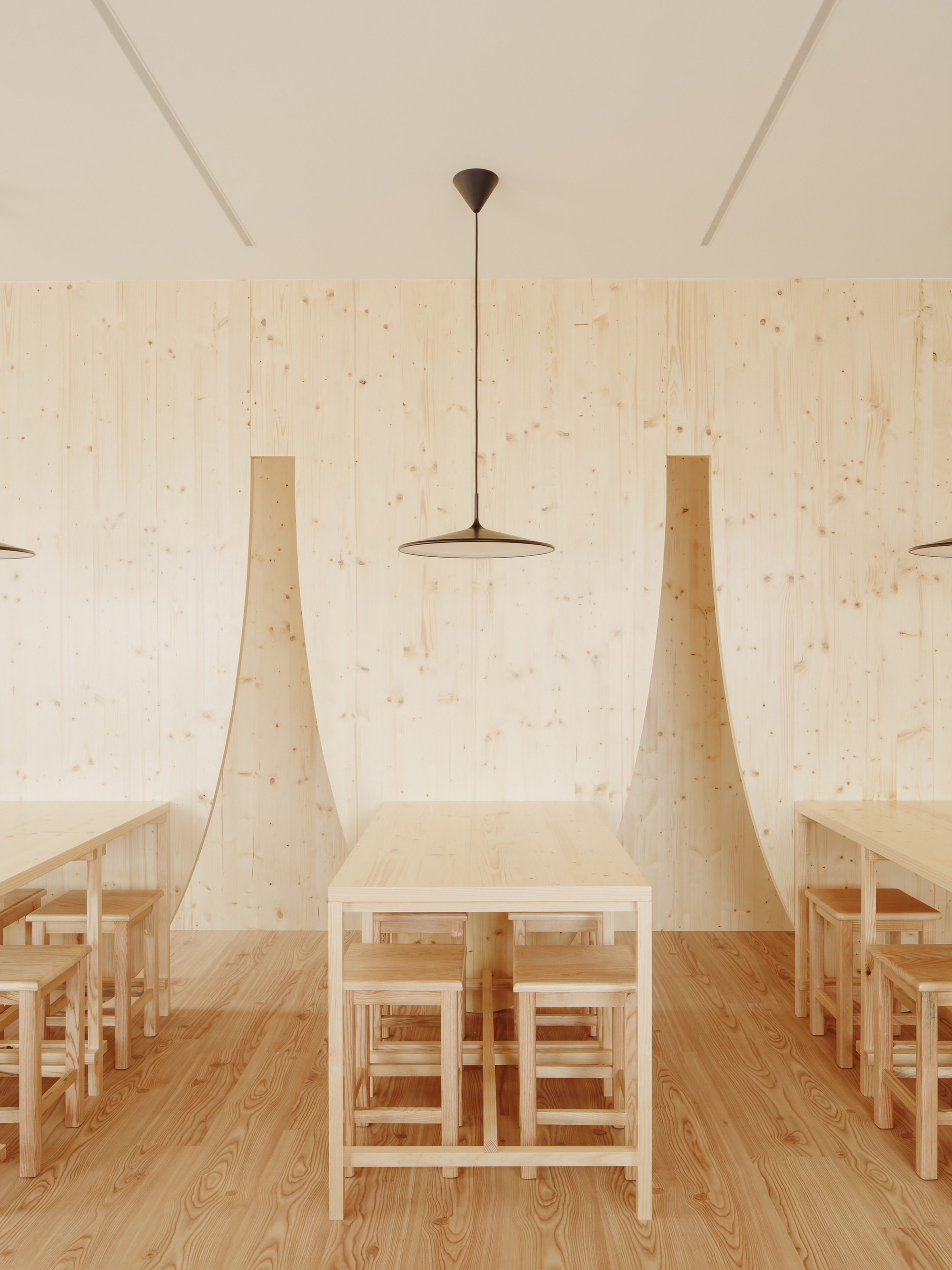 Central dining table flanked by tapered plywood wall fins under a flat disc pendant