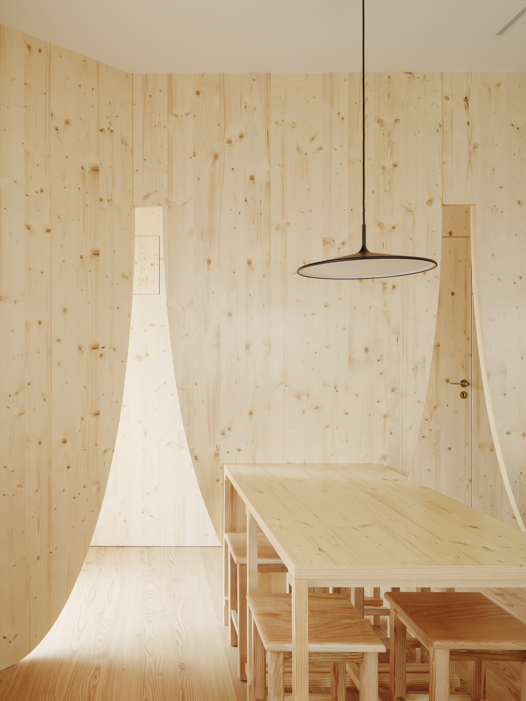 Light wood dining area with tapered chimney form and circular pendant light fixture above