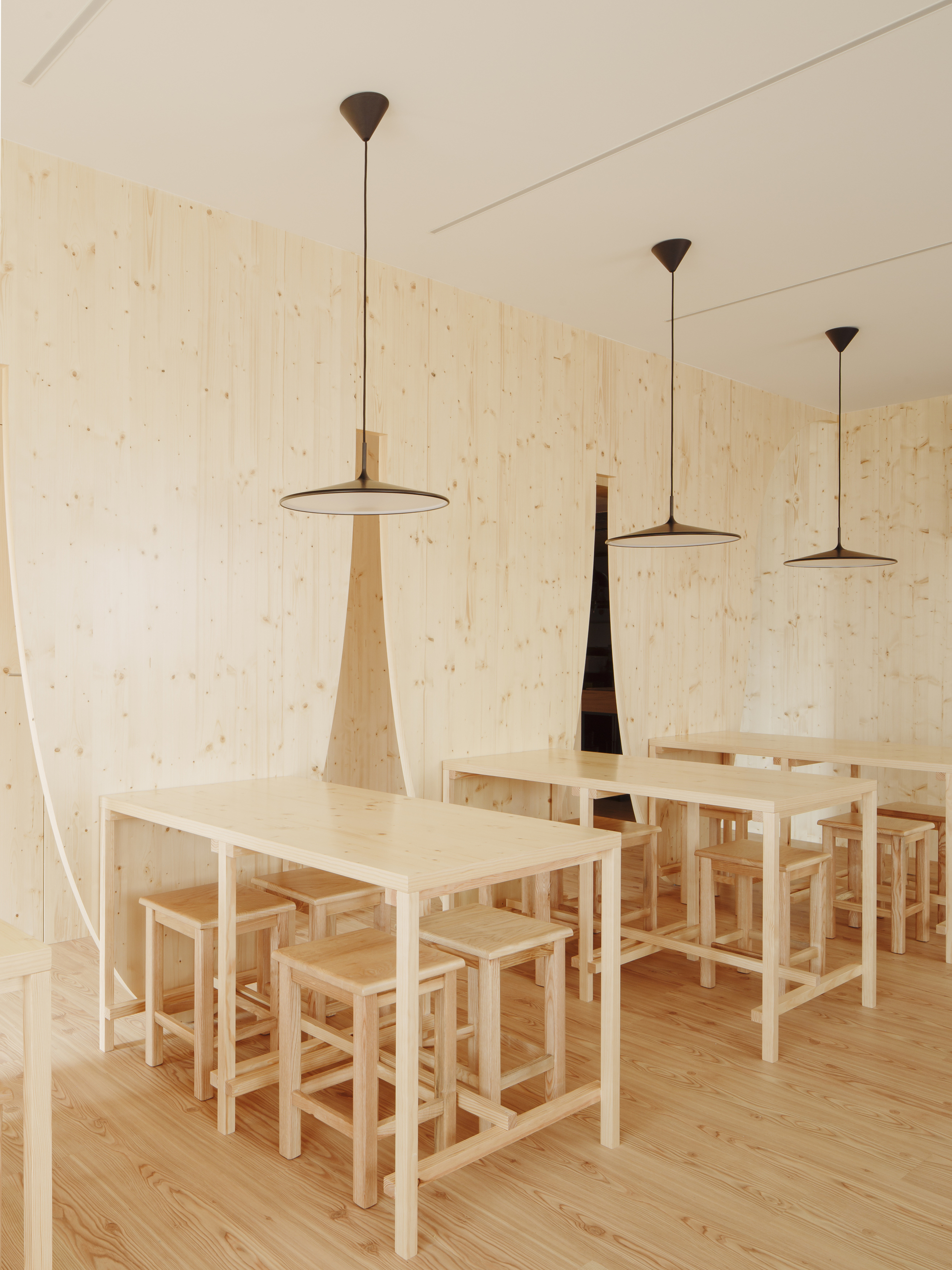 Dining tables and stools arranged beneath three pendant lights and vertical sculptural forms