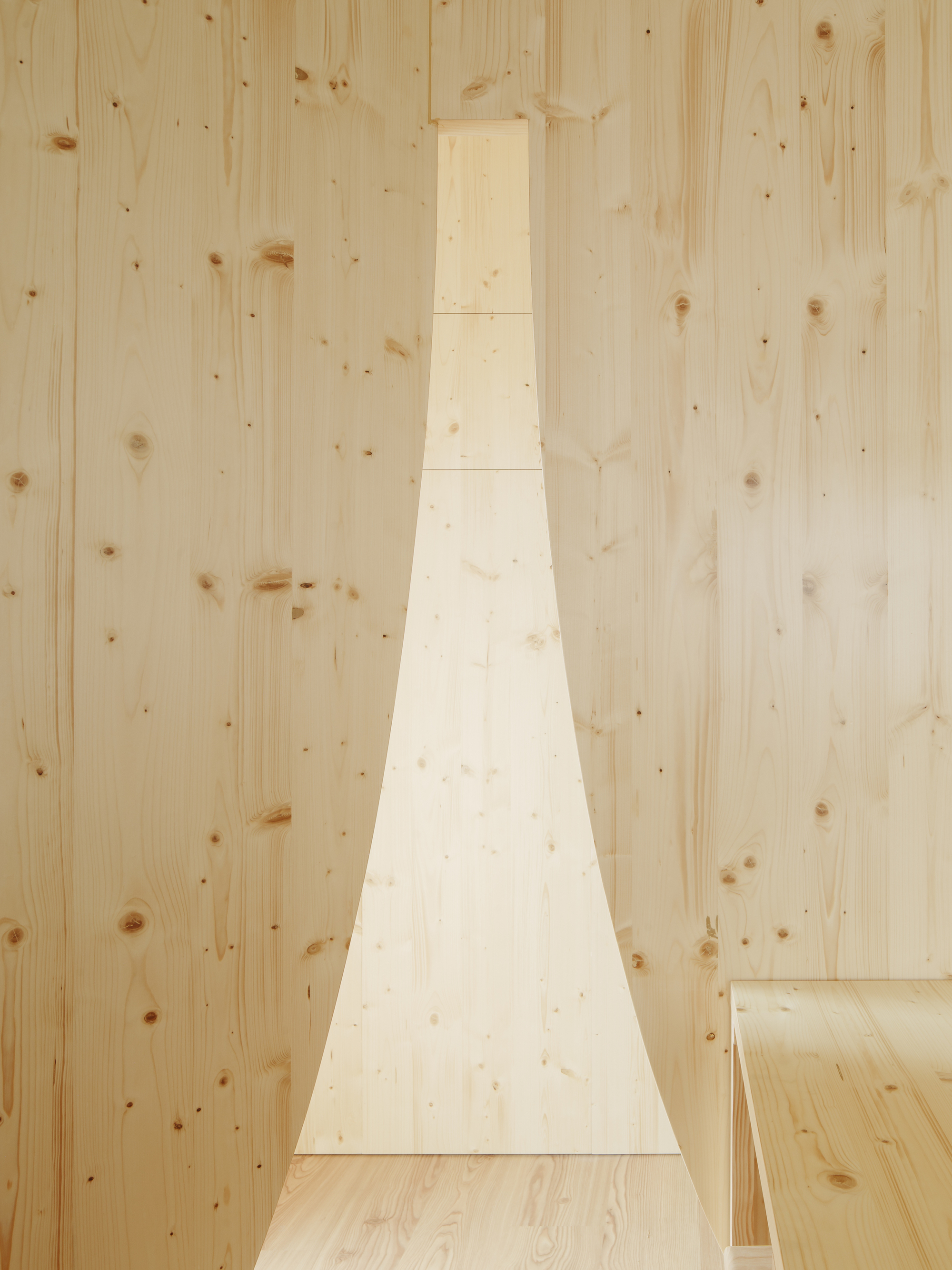 Narrow vertical window cut into pale timber wall beside plywood flooring