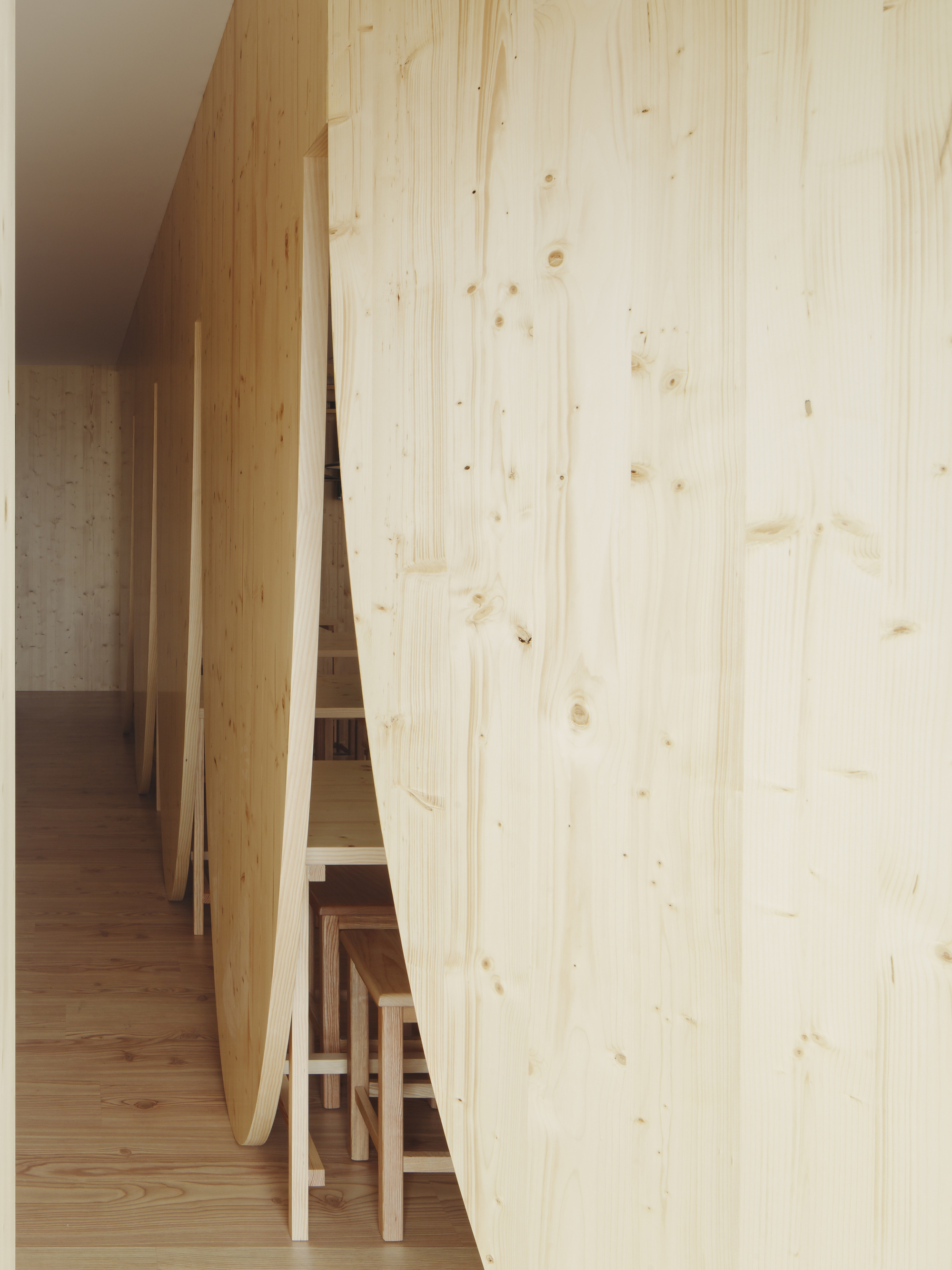 Glimpse through curved partition wall showing stacked stools and concrete in background