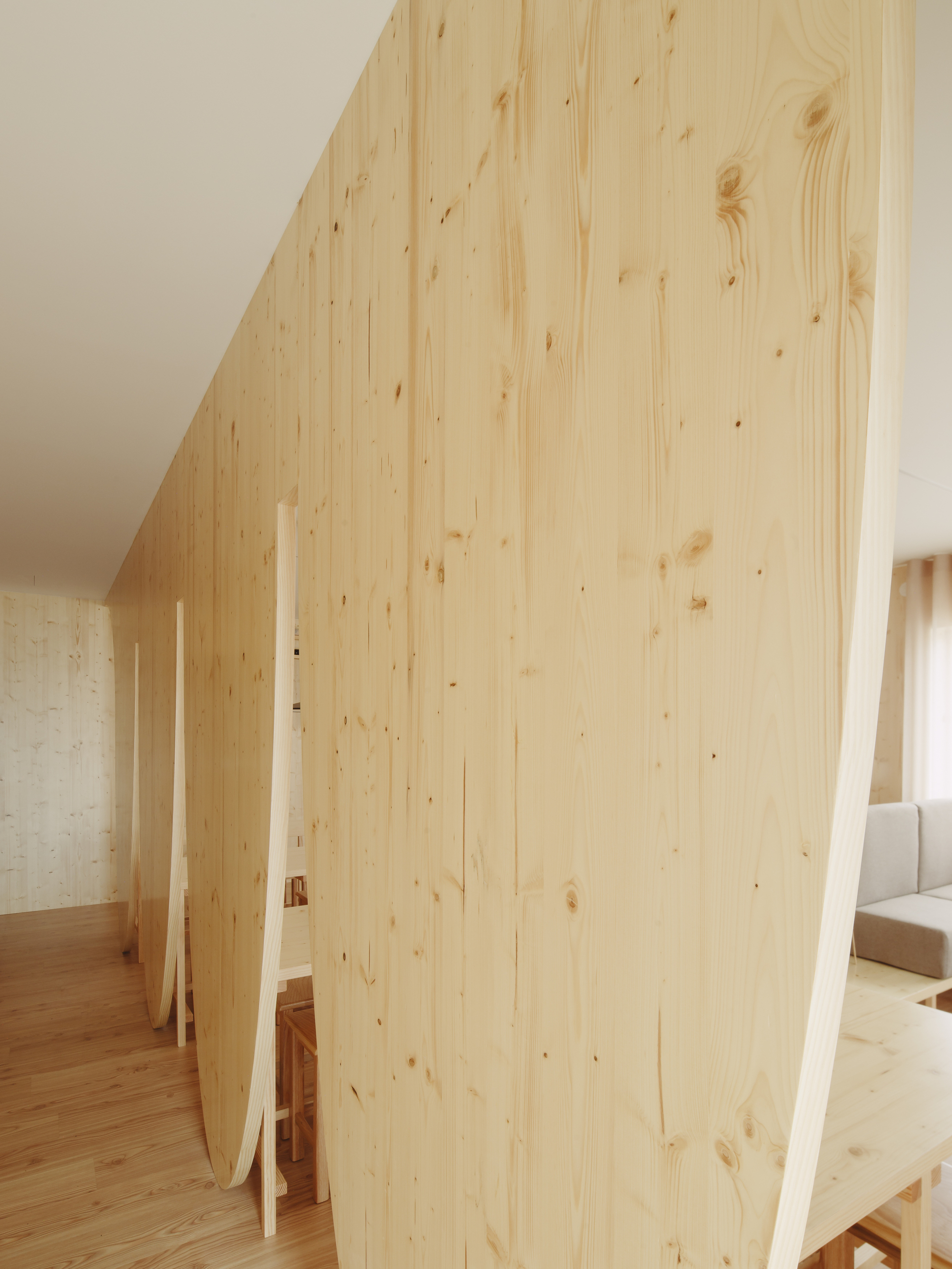 Light wood partition wall with vertical planks curving through an interior with timber flooring
