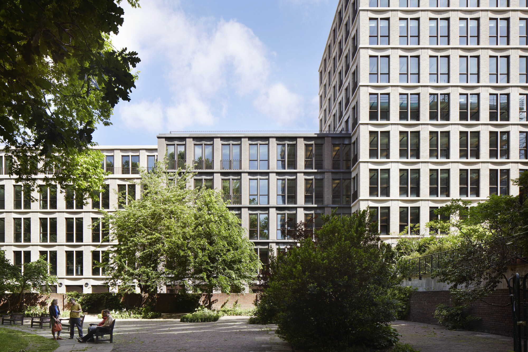 Courtyard view of the gridded window facades framed by mature trees and people on benches