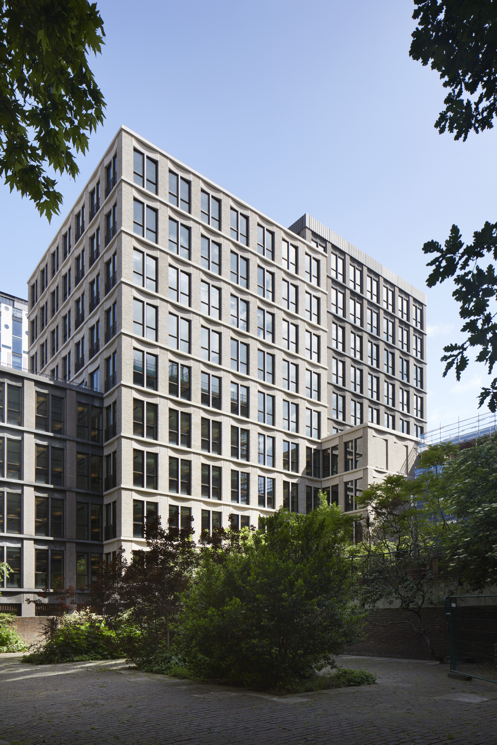 Multi-story facade with regular window grid and planted landscaping framed by tree canopy