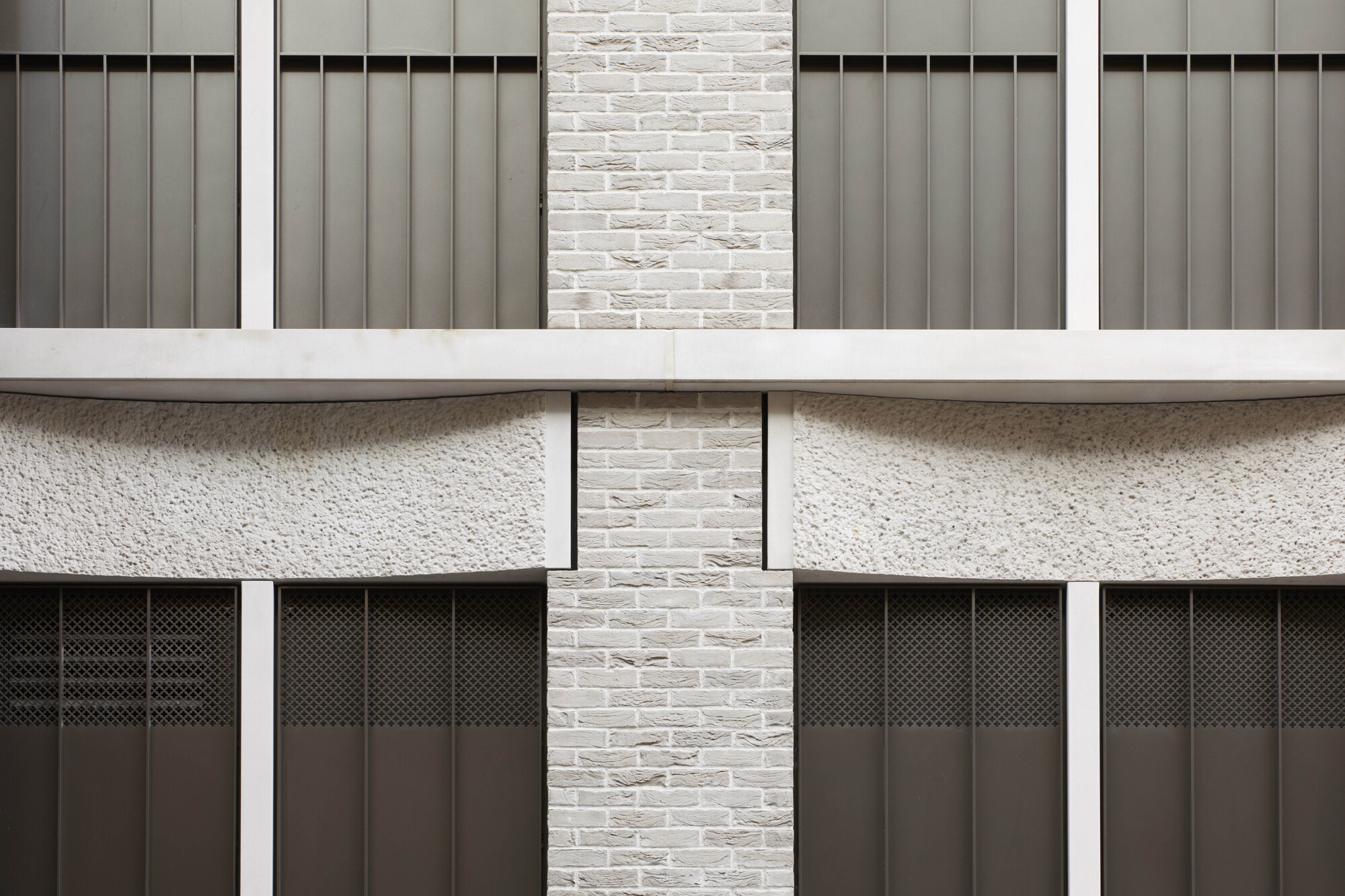 Facade detail showing white brick piers between grey metal panels and scalloped concrete spandrels