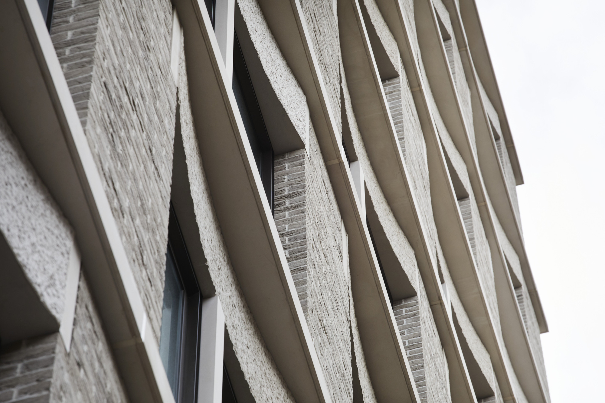 Angled view of the textured brick facade with projecting balcony fins under overcast skies