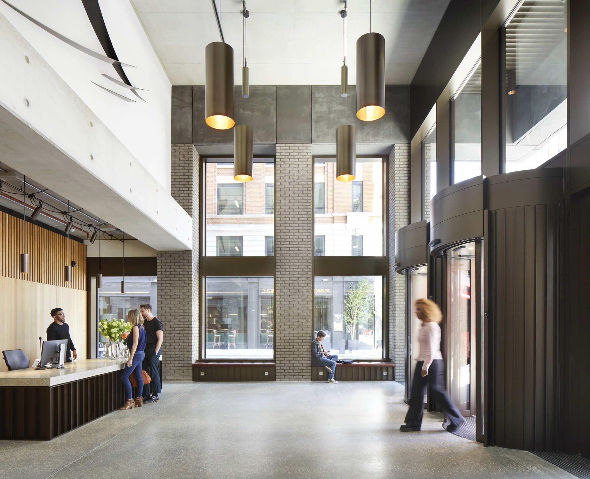 Double-height reception lobby with cylindrical bronze pendant lights and floor-to-ceiling windows overlooking the street
