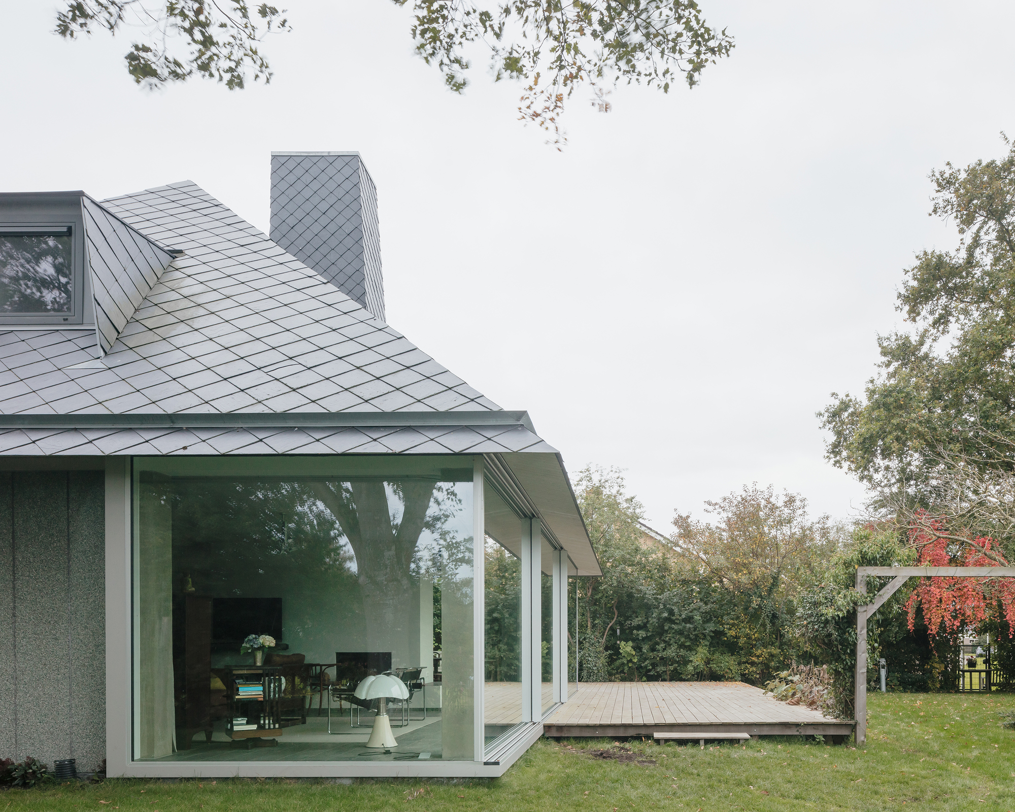 Garden facade with full-height glazing opening onto a timber deck under overcast skies