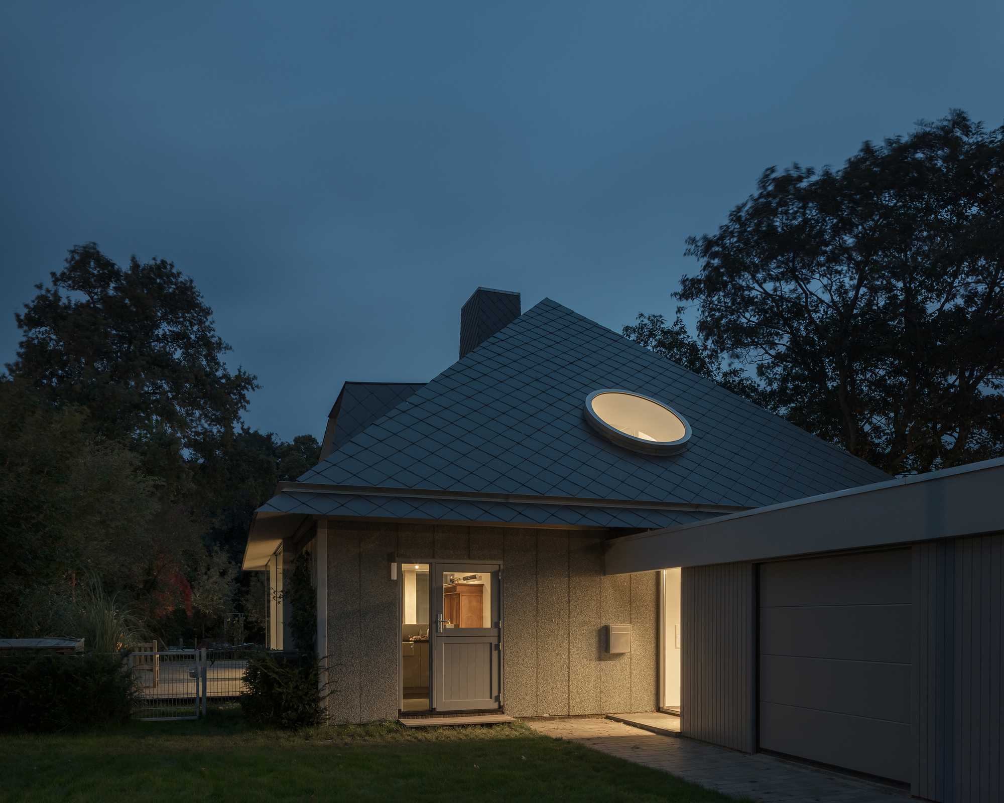 Entry facade with circular roof light above the glazed door at twilight