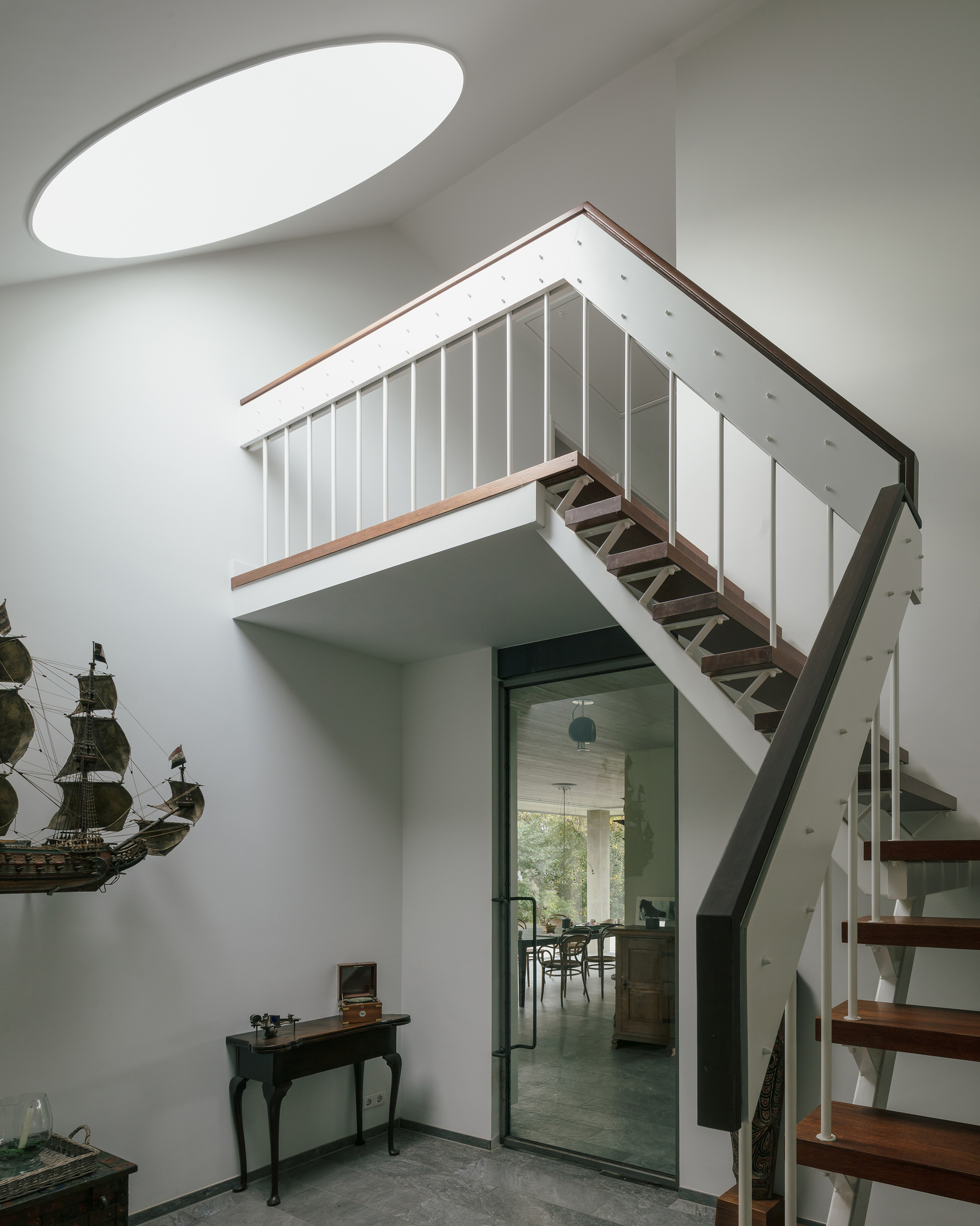 Interior staircase with timber treads and white vertical railings beneath an oval skylight