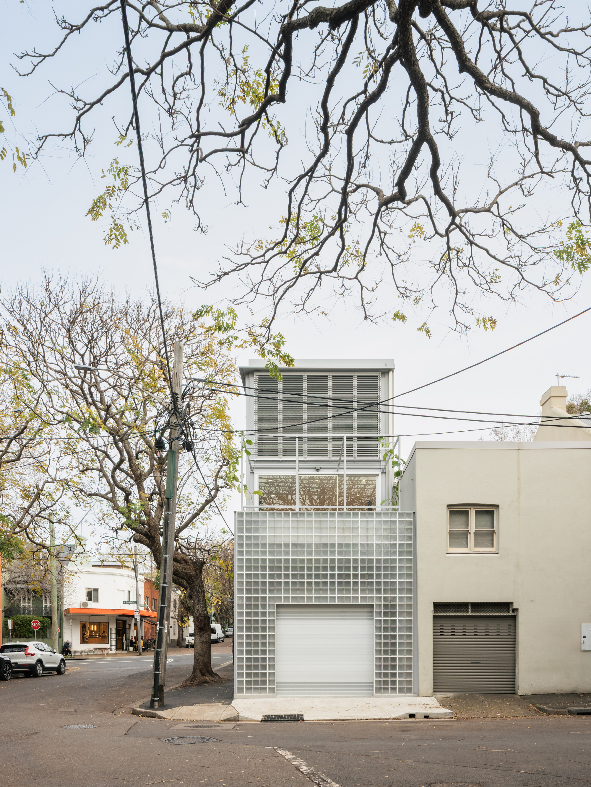 Front elevation showing stacked glass block volumes with louvered upper windows beneath bare branches