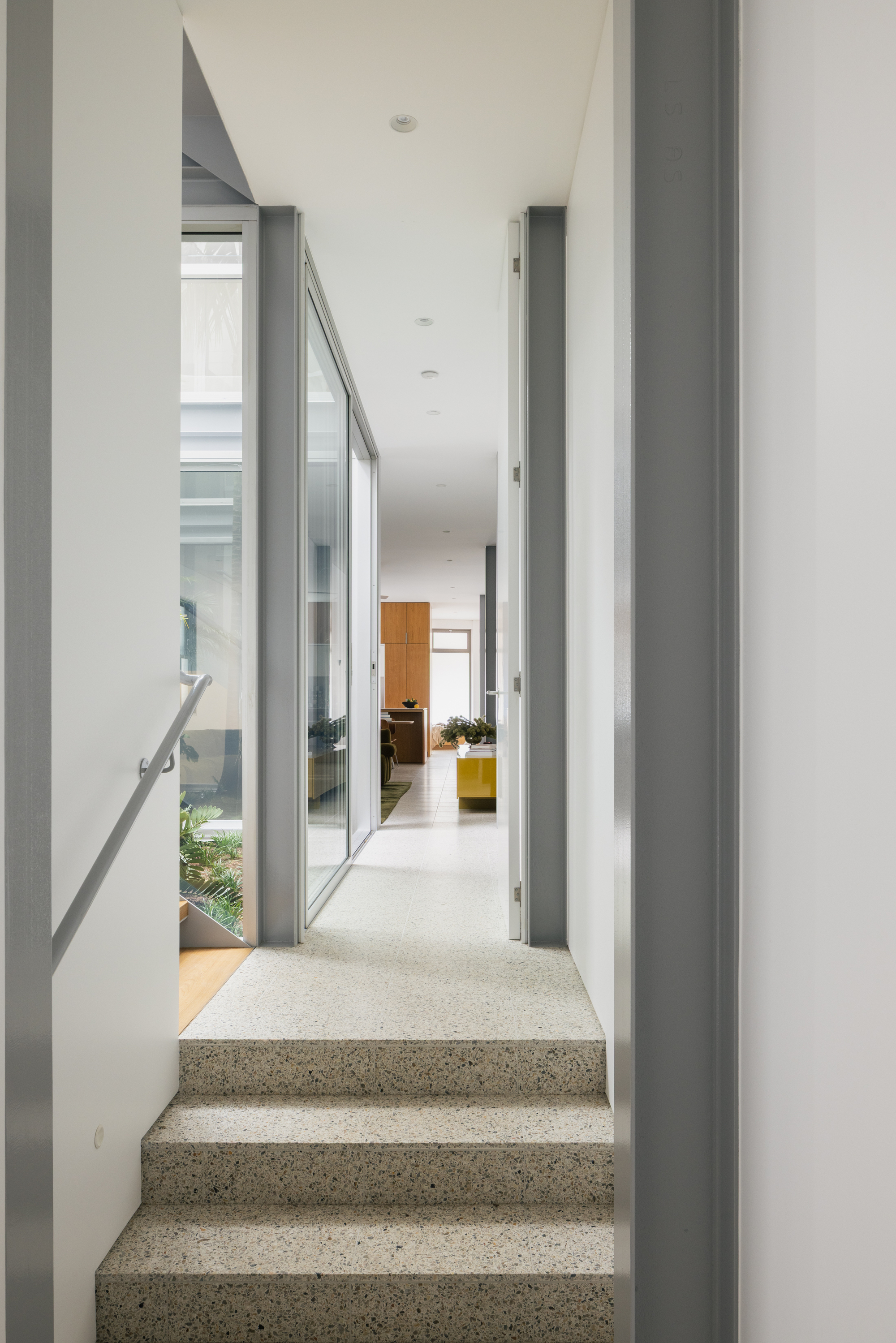 Split-level stairs with terrazzo treads leading up through a narrow corridor with glazed courtyard