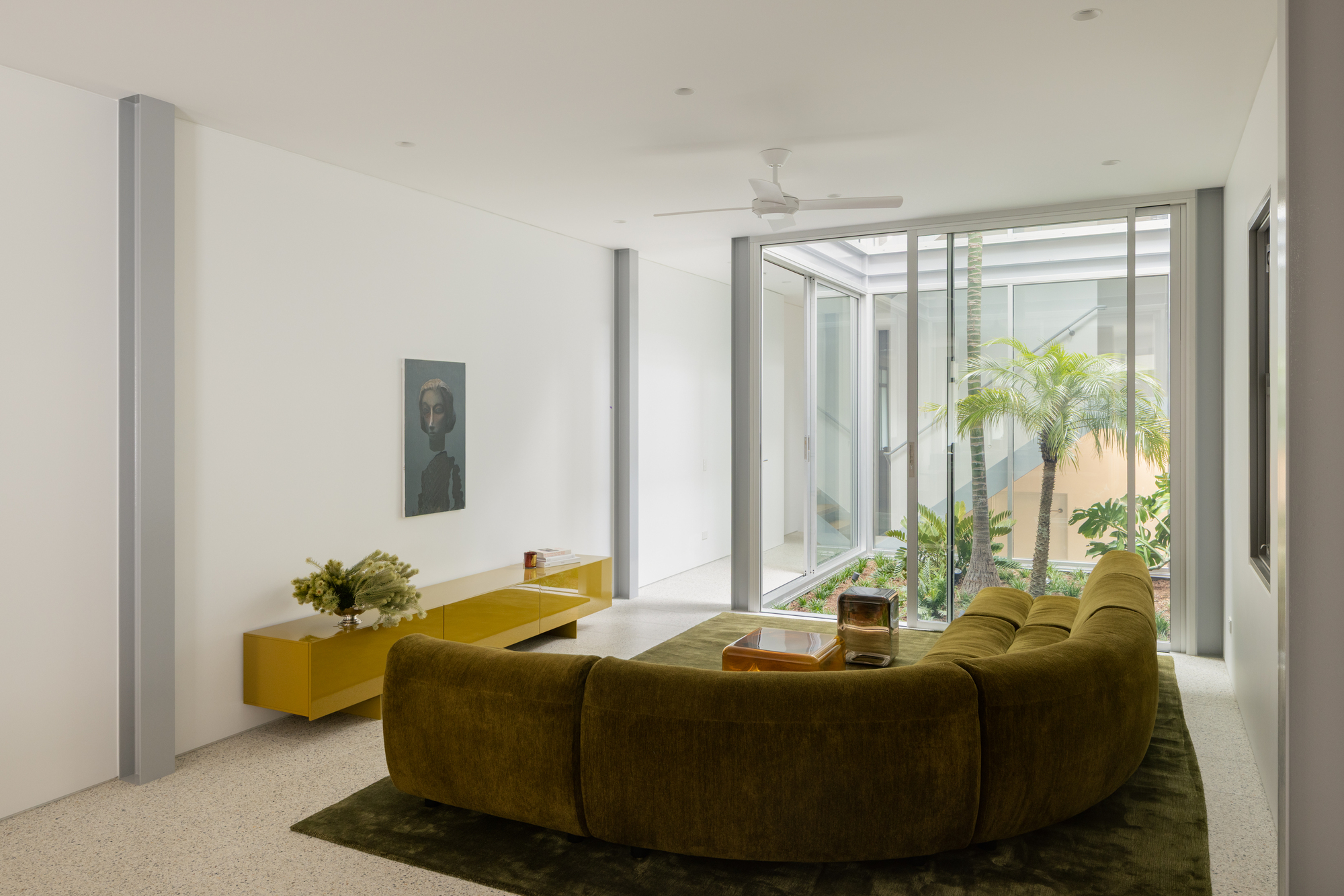 Living room with terrazzo floor opening onto a glazed courtyard planted with palms