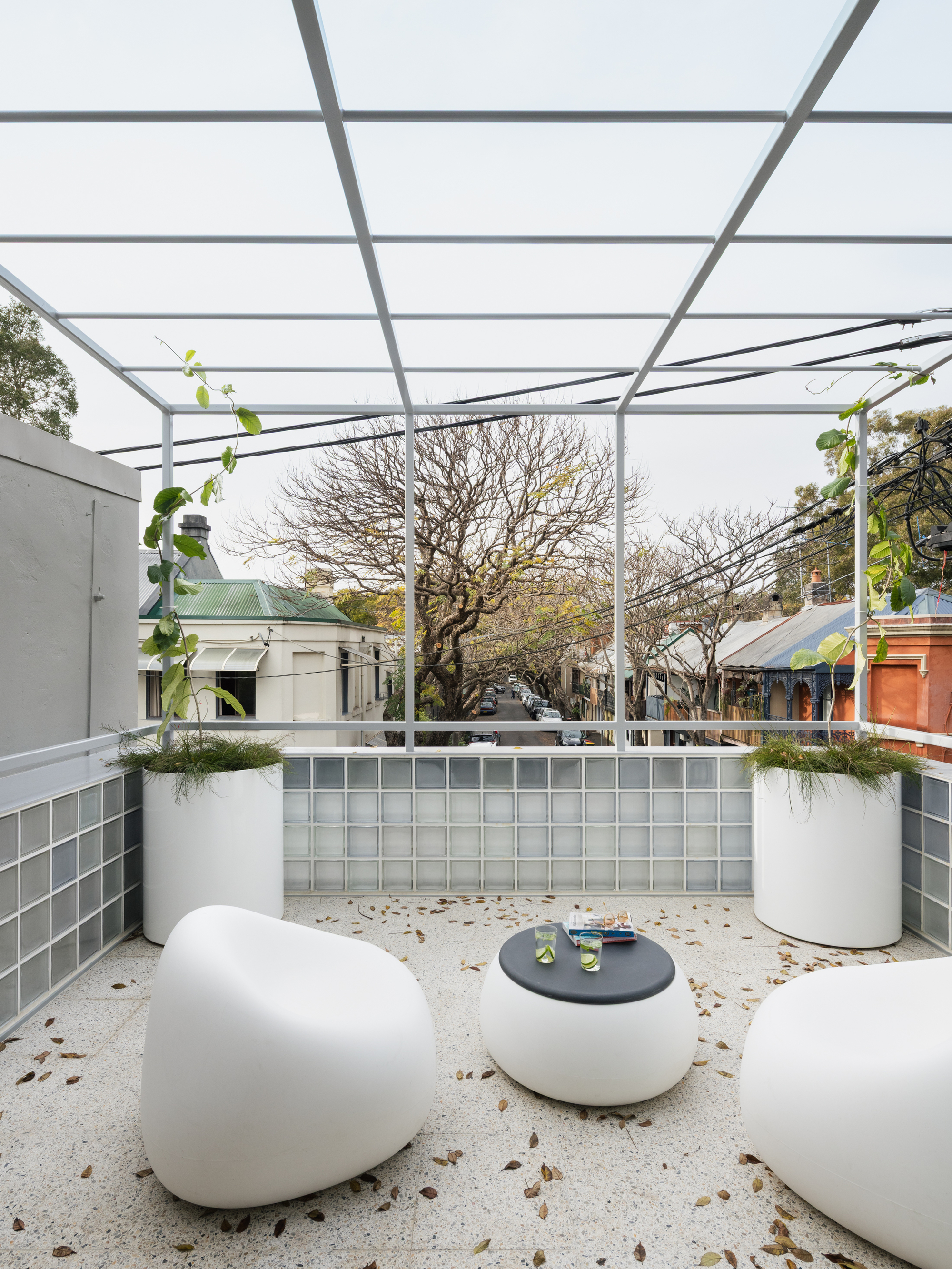 Outdoor courtyard with steel pergola overhead, glass block parapet and terrazzo floor scattered with leaves