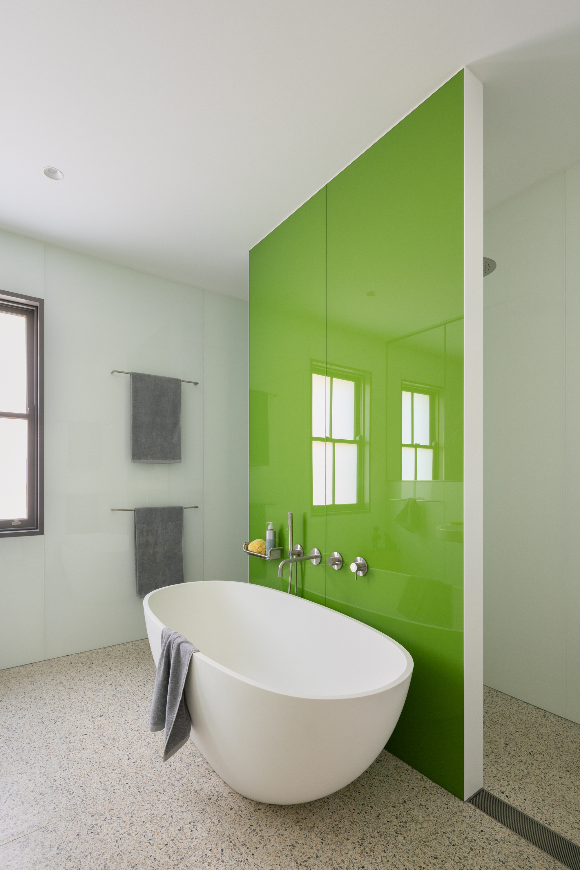 Freestanding bathtub positioned against a lime green glass wall with wall-mounted faucets