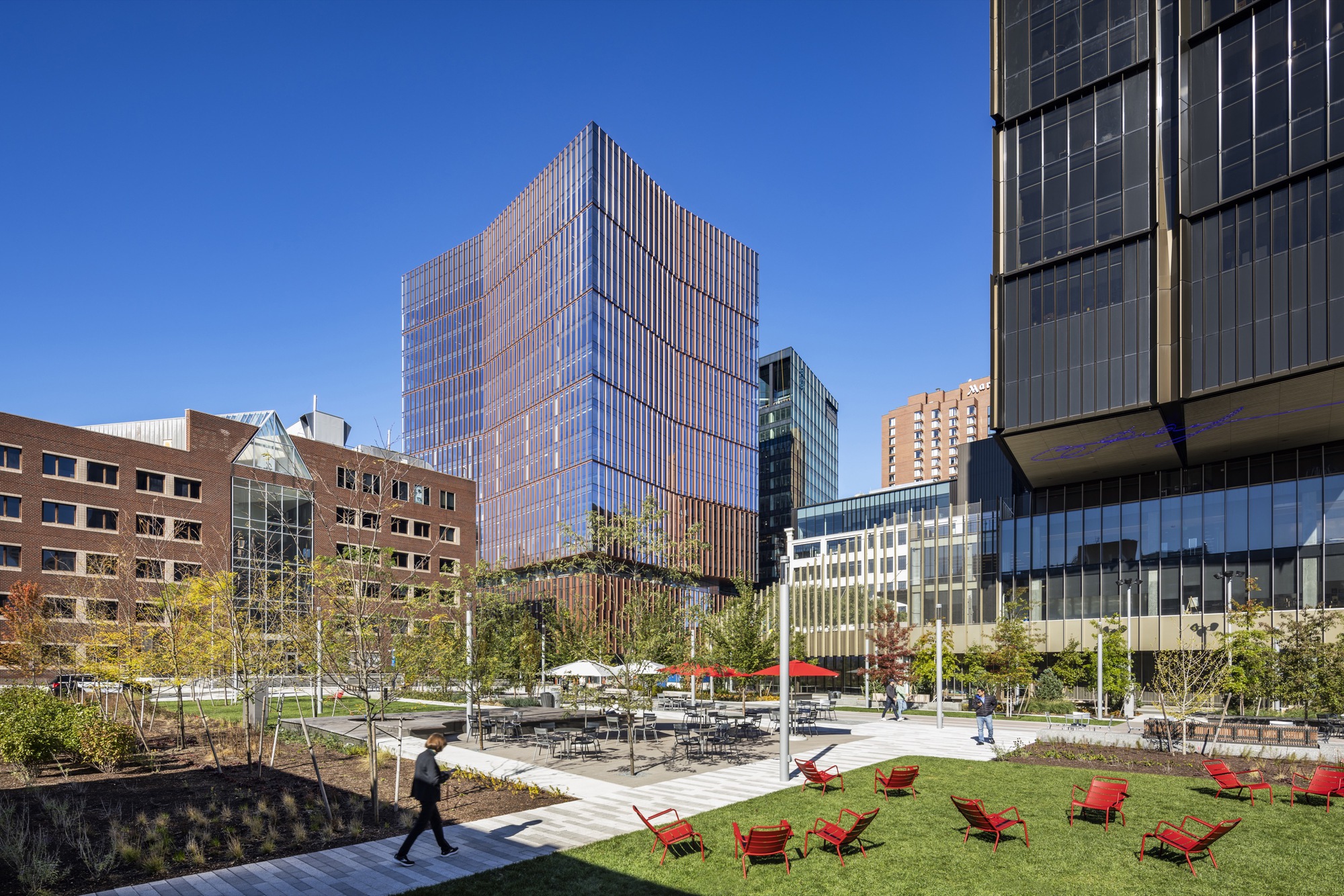 Public plaza with red lounge chairs on lawn and surrounding residential and office towers under blue sky