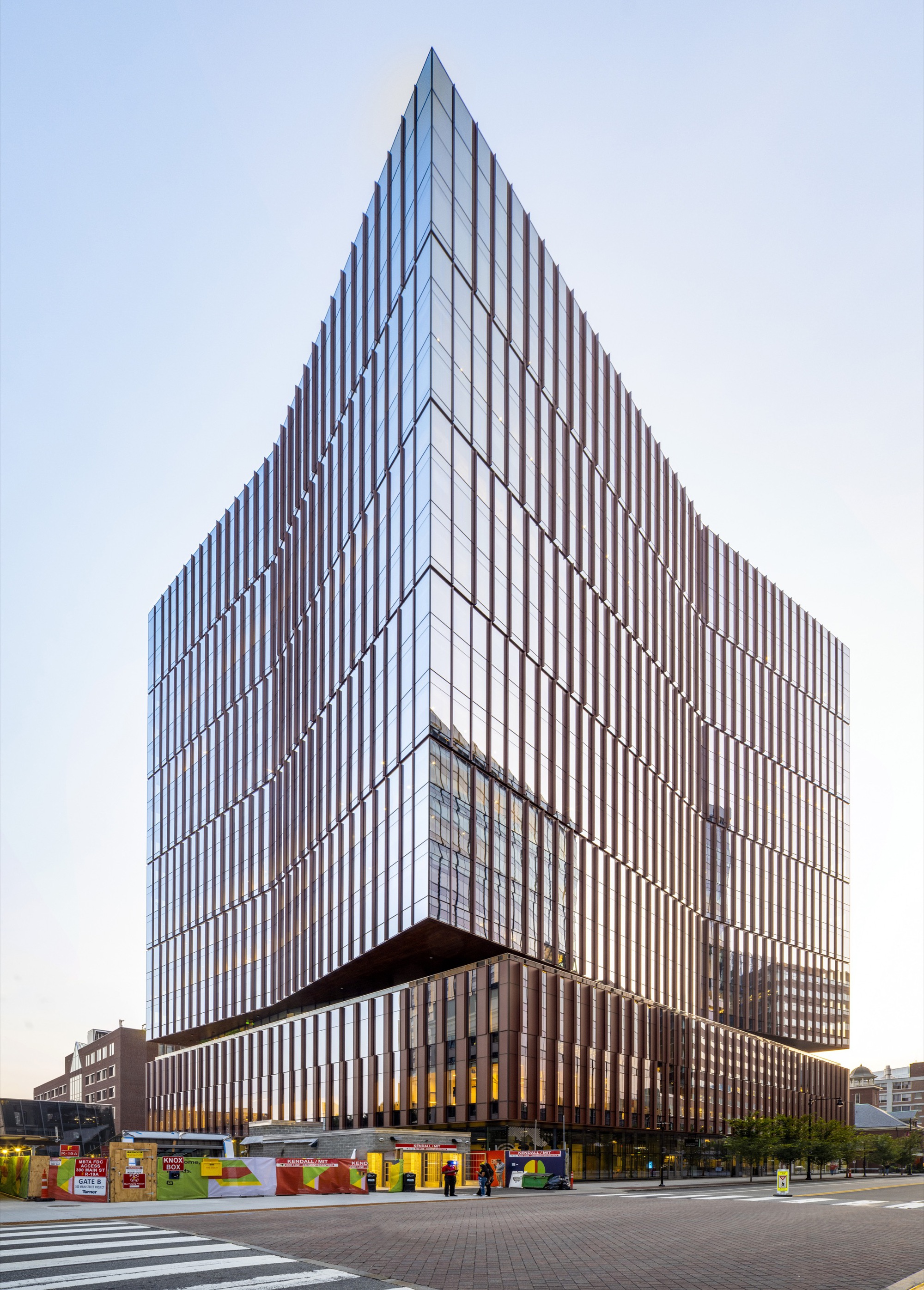 Corner view of the tower showing vertical metal fin facade and cantilevered podium above street level