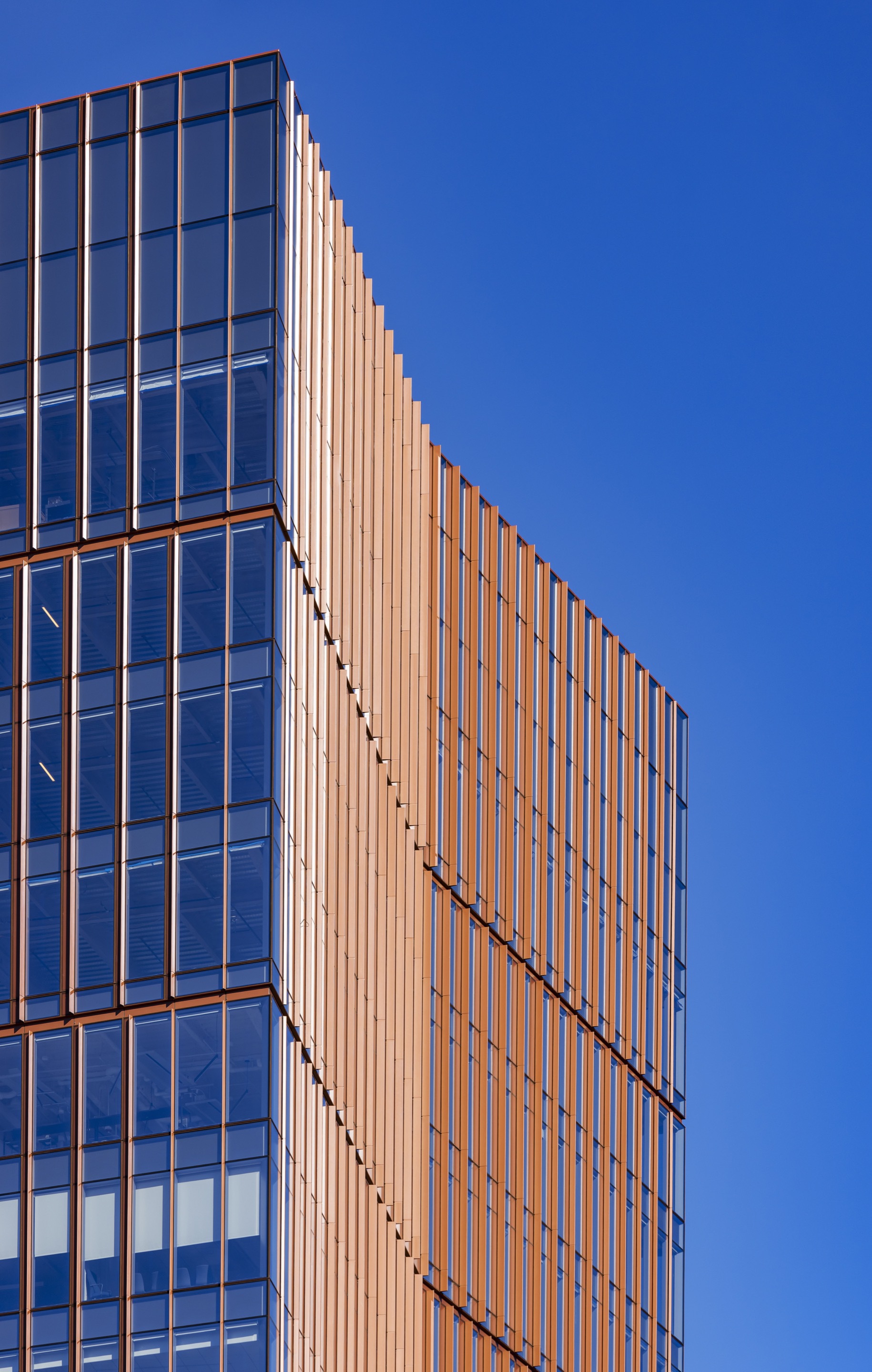 Close-up of the tower corner with bronze vertical fins against glass curtain wall and clear blue sky
