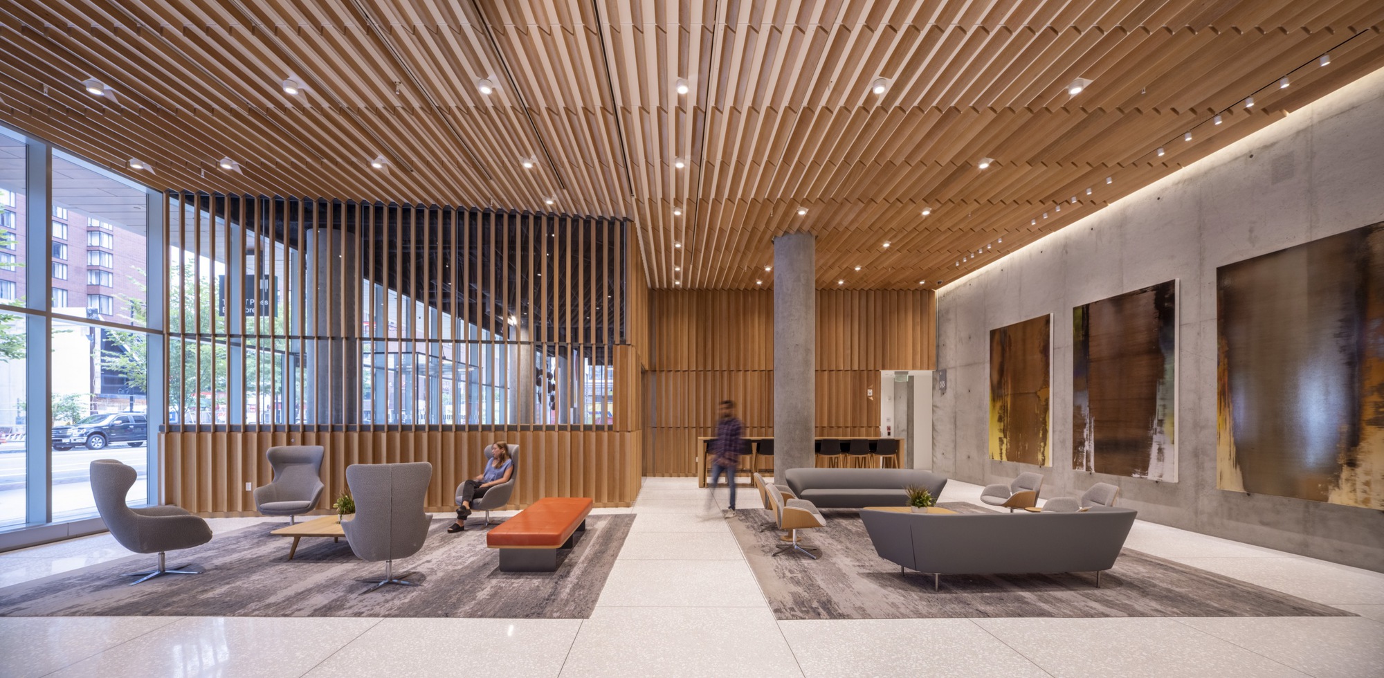 Double-height lobby with slatted wood ceiling, concrete walls and seating groups with two figures visible