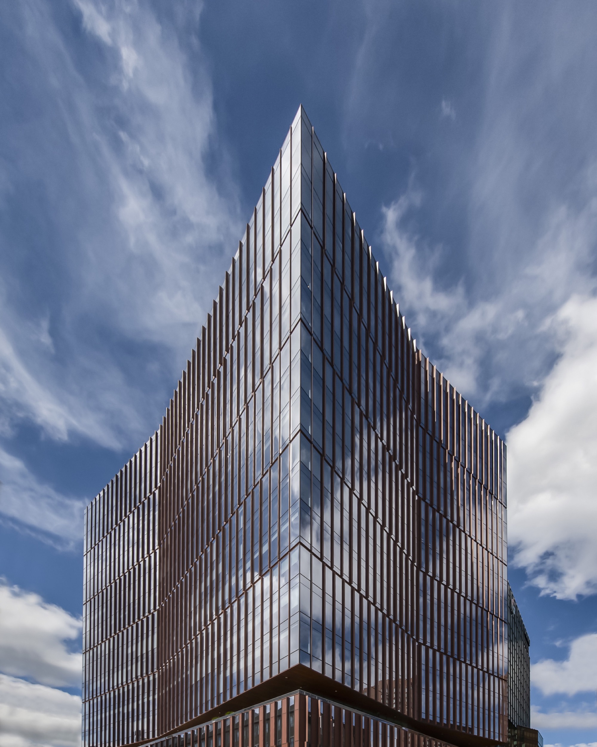 Tower facade with vertical bronze mullions and glazed curtain wall under a partly cloudy sky