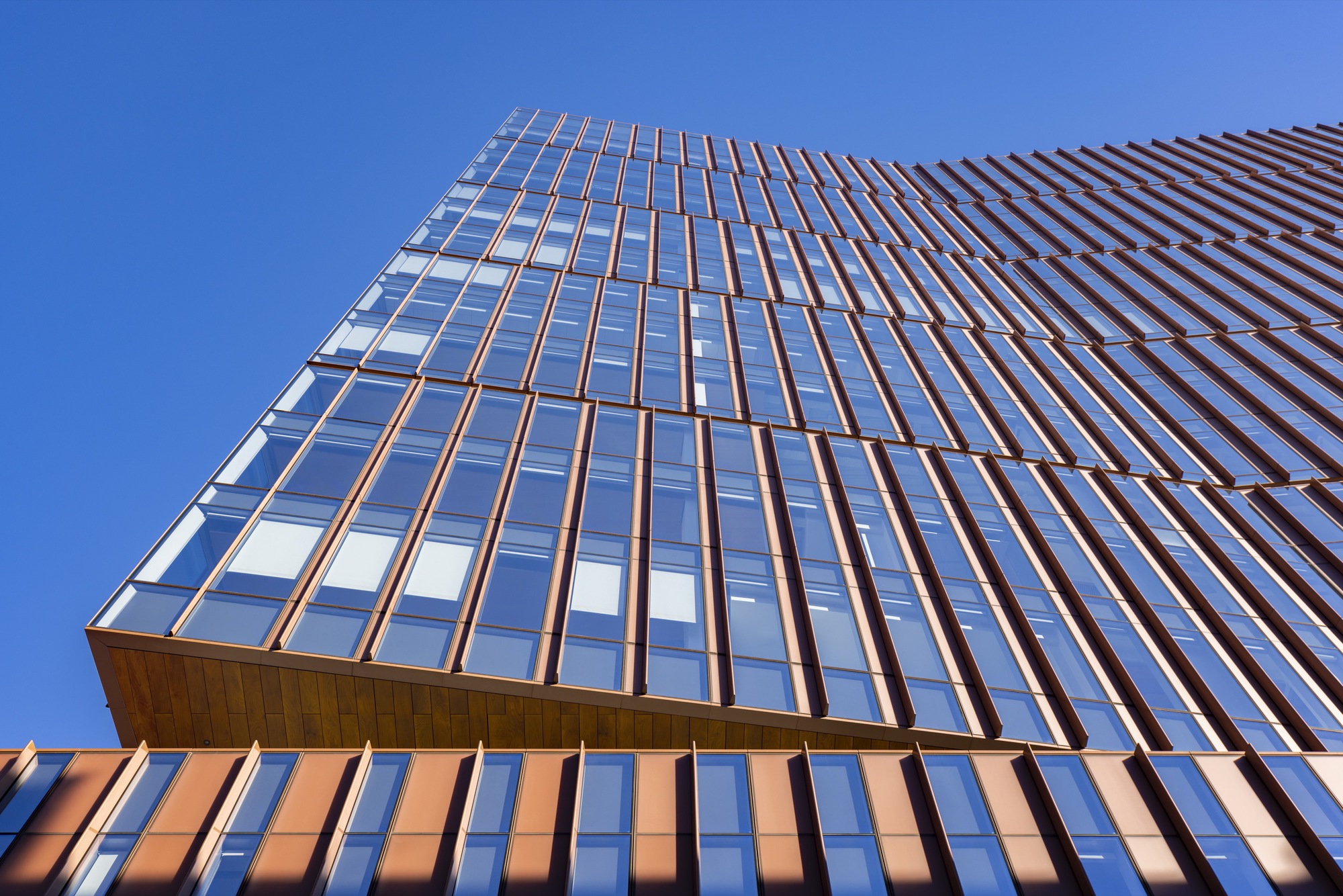 Upward view of the glazed tower facade with bronze vertical fins against a clear blue sky