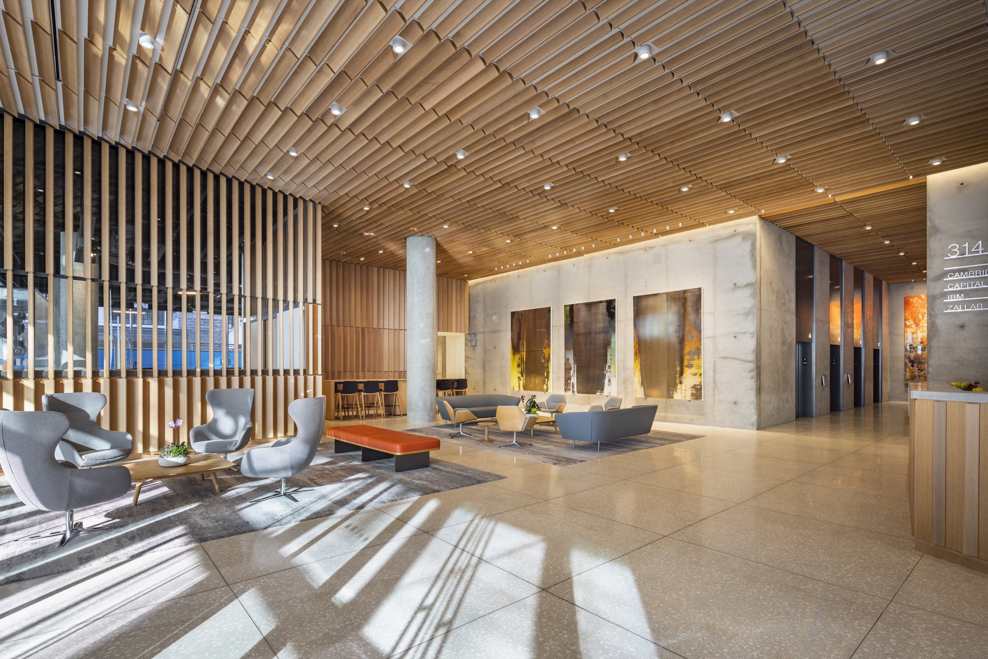 Lobby with slatted timber ceiling, concrete and marble walls, and sunlight patterns on the polished stone floor