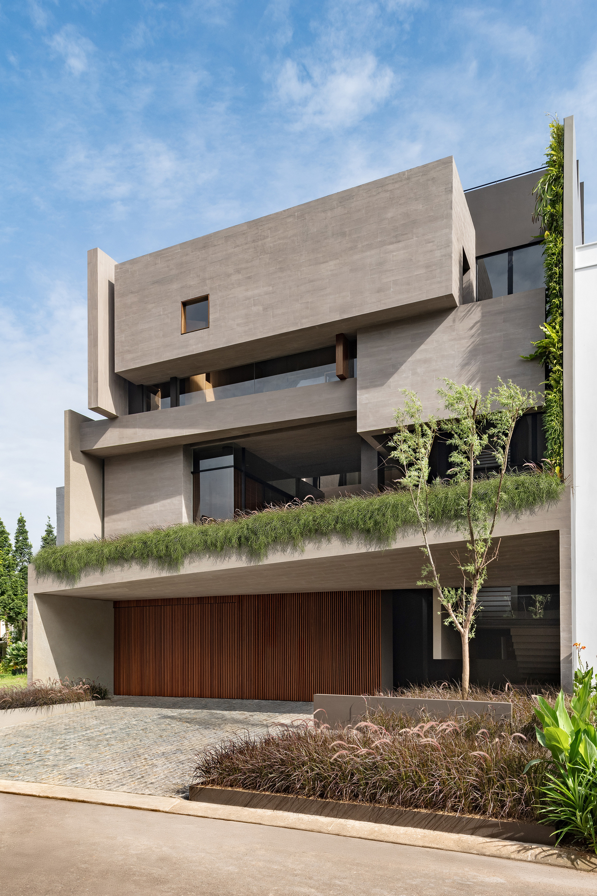 Stacked concrete volumes with planted terraces and vertical garden wall under a blue sky