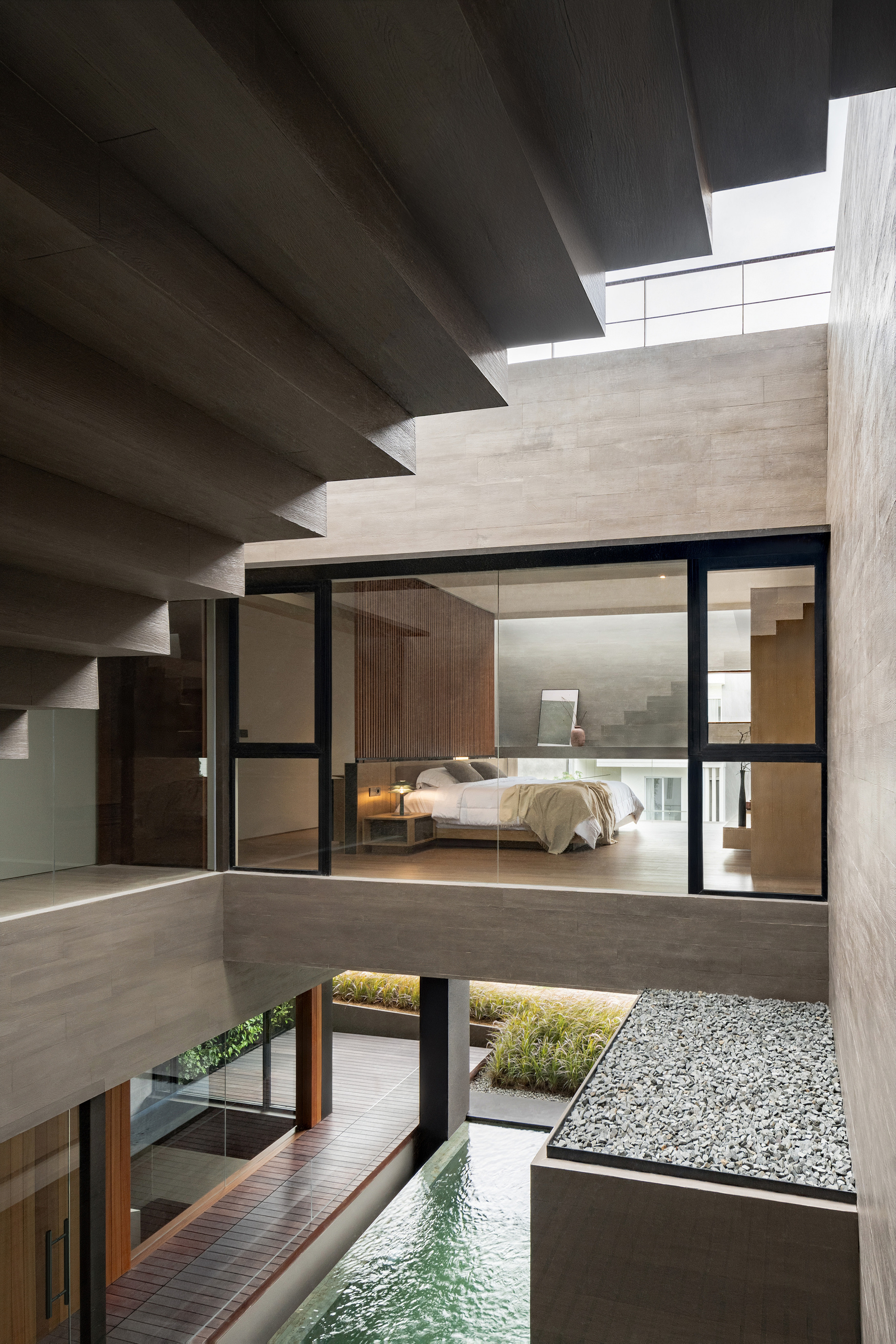 Multilevel interior courtyard showing concrete staircase, glazed bedroom and white pebble garden bed