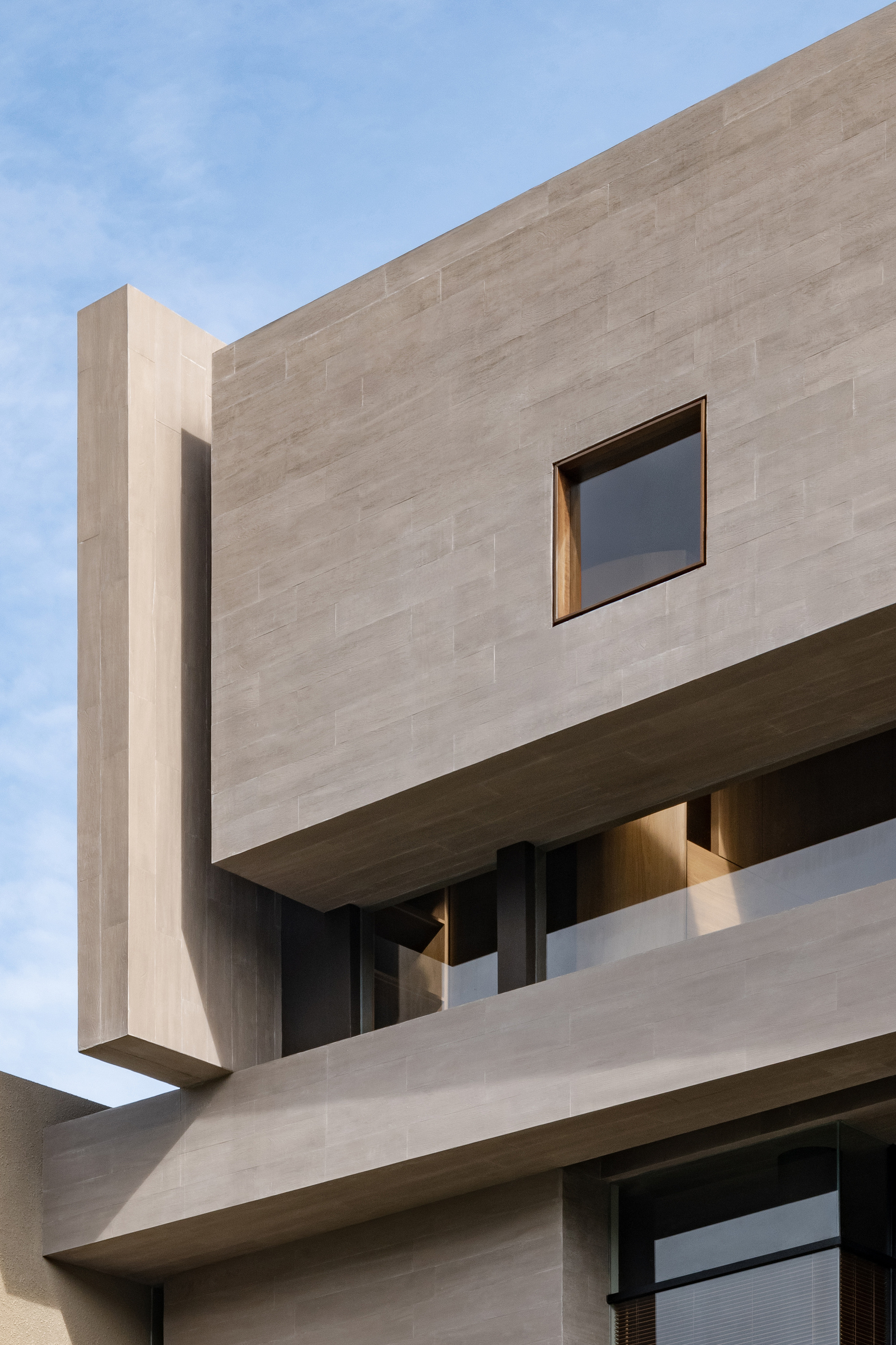 Upper facade detail showing cantilevered concrete volume with square window and recessed glazing below