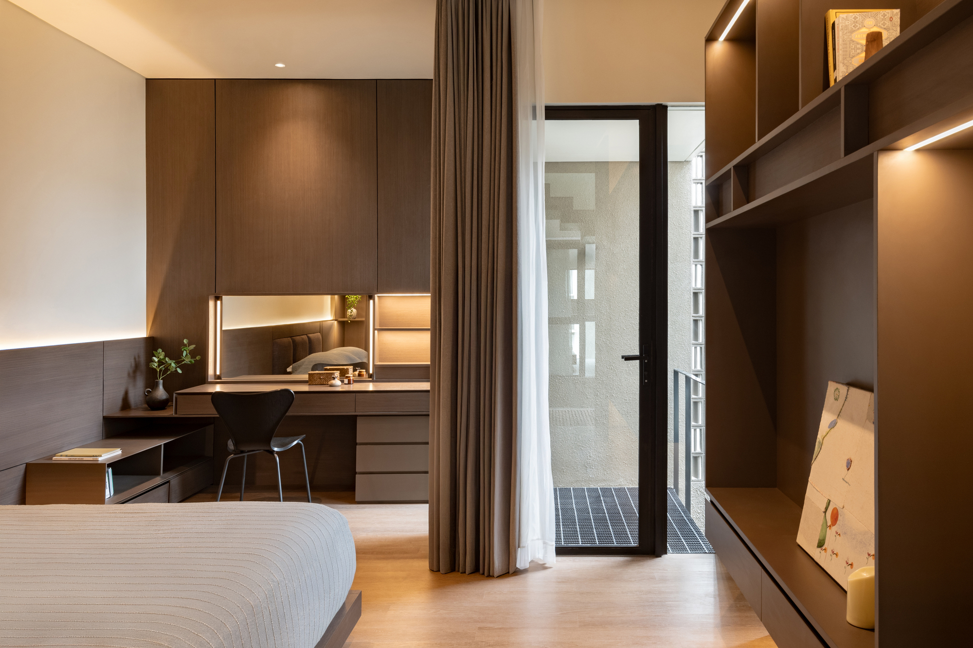 Bedroom with built-in desk and shelving leading to a narrow glass-brick lightwell beyond curtains