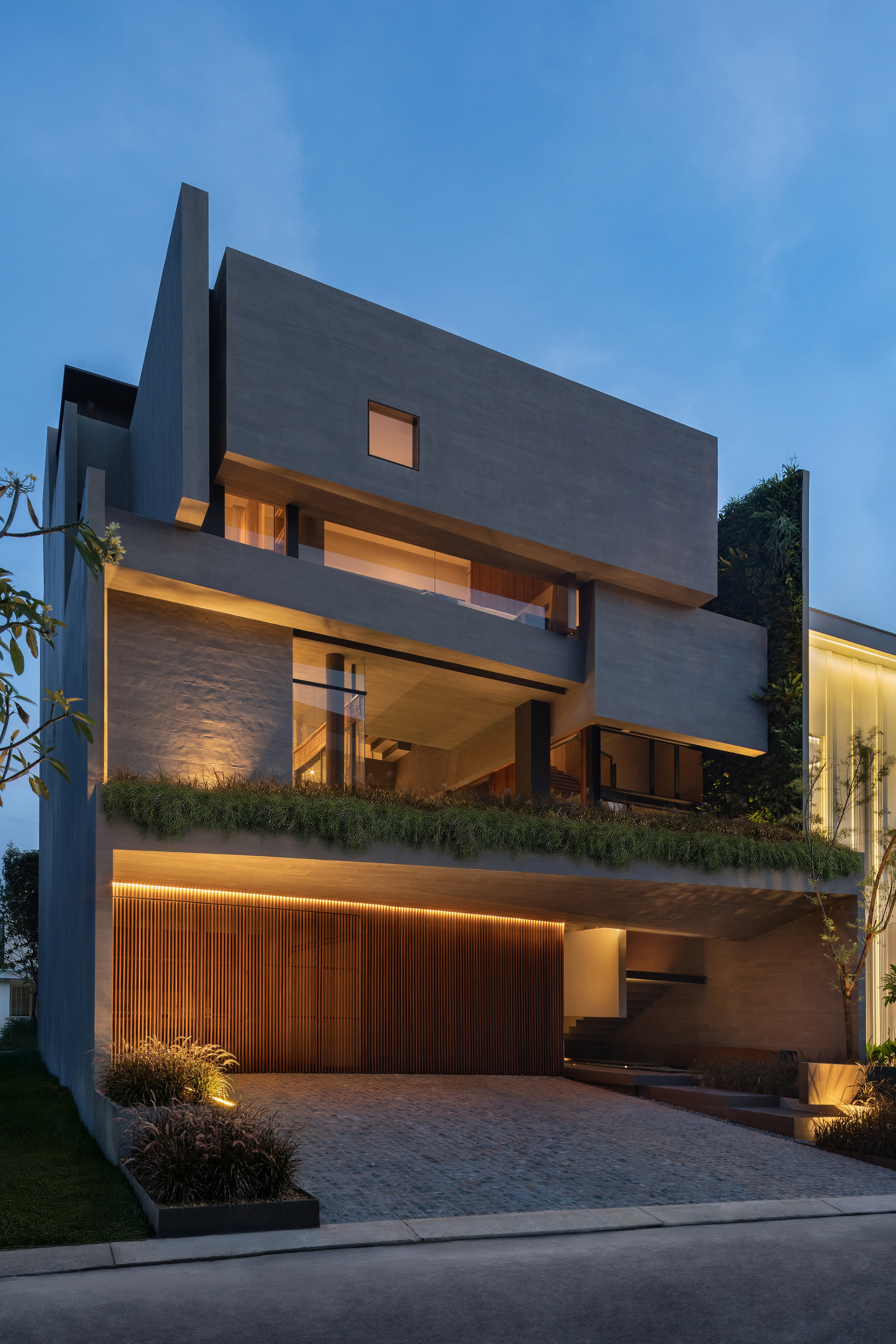 Street facade at dusk showing stacked volumes with planted balconies and timber-clad garage level