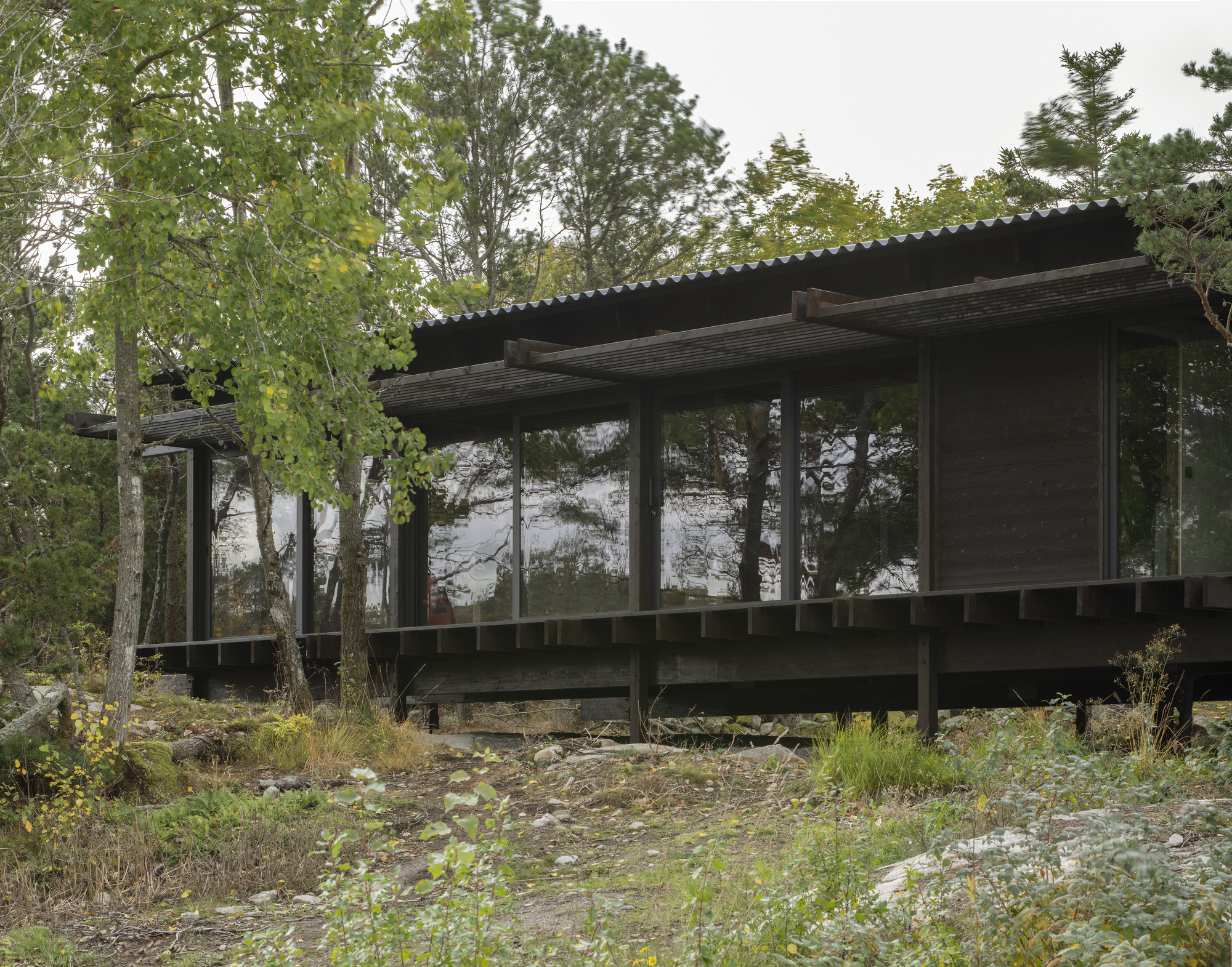 Lakeside elevation showing the raised timber deck and full-height glazing beneath the corrugated metal overhang